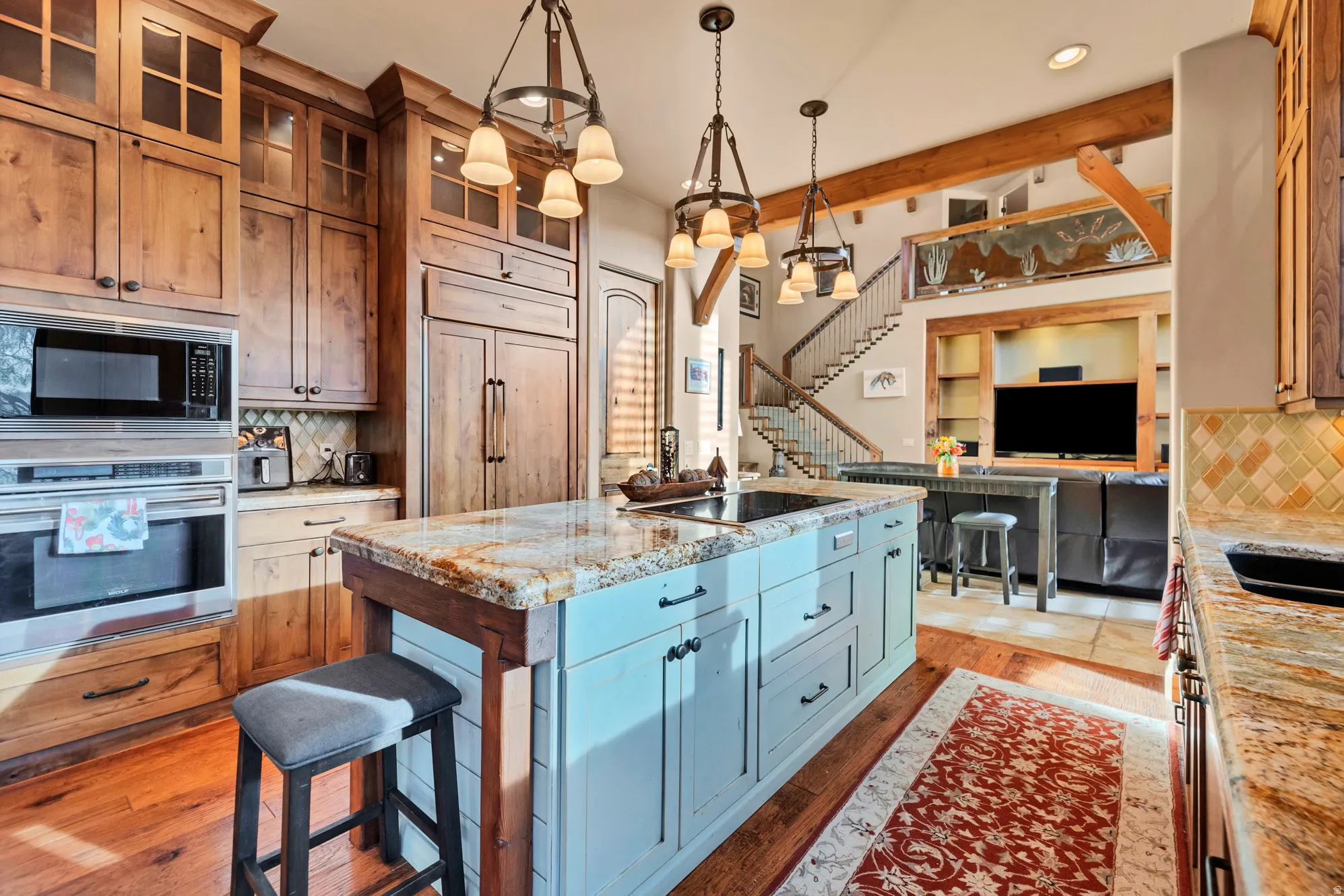 Kitchen featuring decorative backsplash, a kitchen island with sink, light stone counters, built in appliances, and light wood-style floors