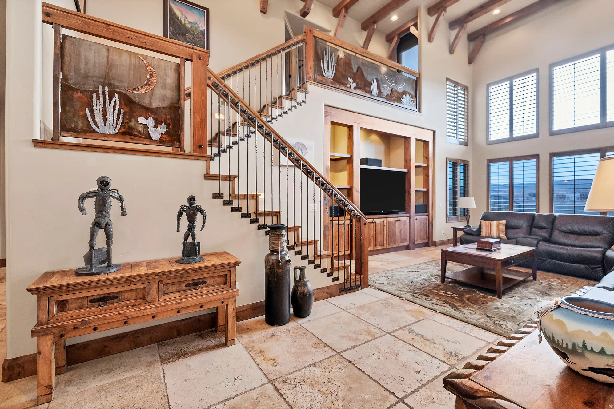 Living area with a towering ceiling, beamed ceiling, stone tile floors, built in shelves, and stairs