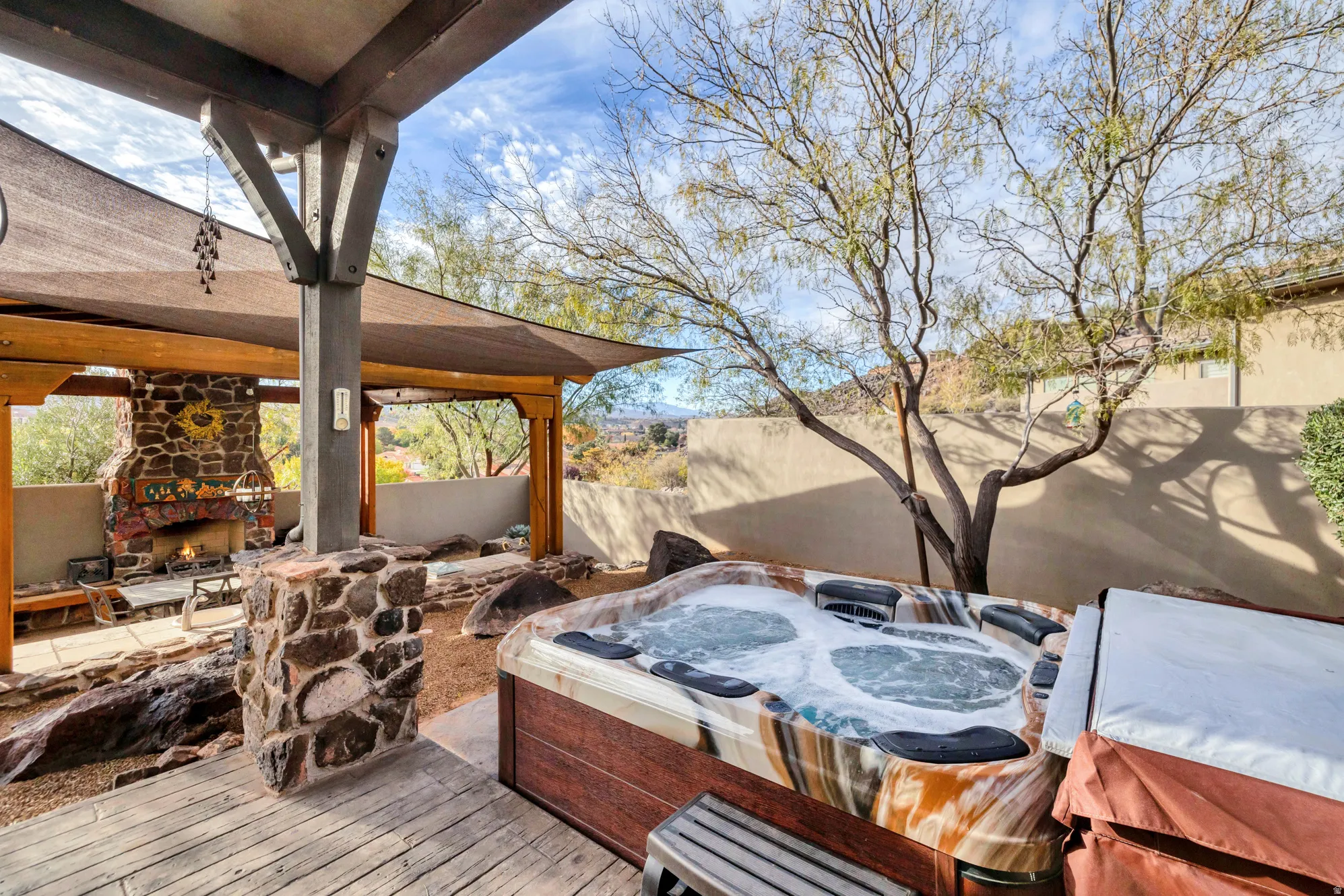 Wooden deck featuring a hot tub, an outdoor stone fireplace, and a fenced backyard