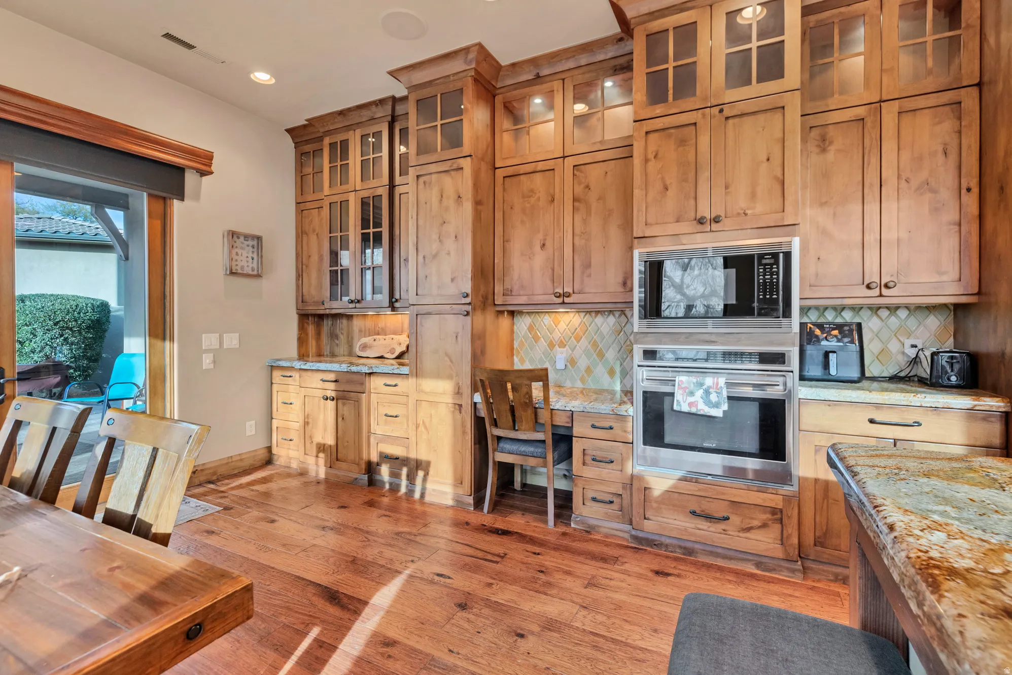 Kitchen featuring oven, glass insert cabinets, light stone counters, black microwave, and backsplash