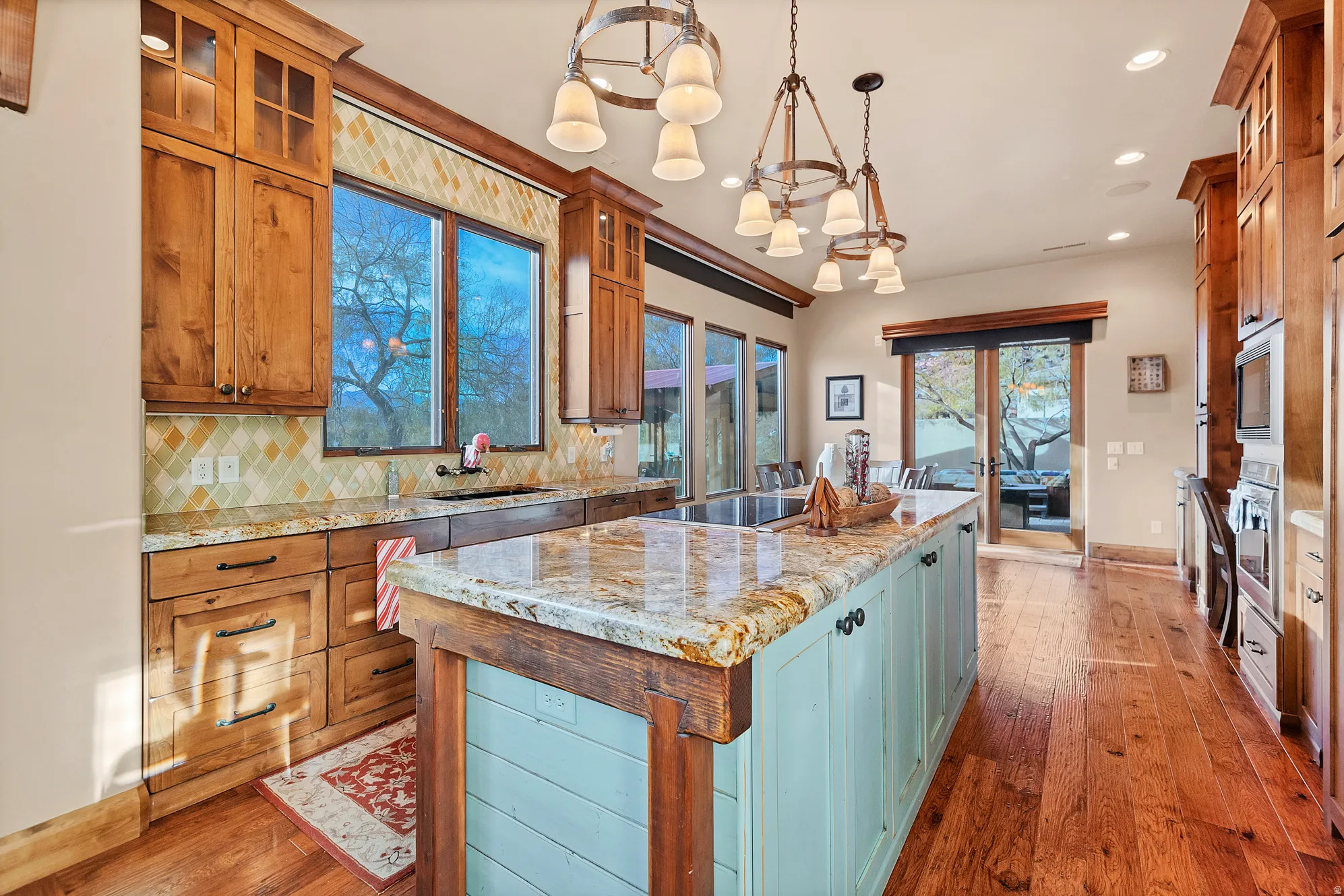 Kitchen with light stone countertops, a center island, decorative backsplash, glass insert cabinets, and decorative light fixtures