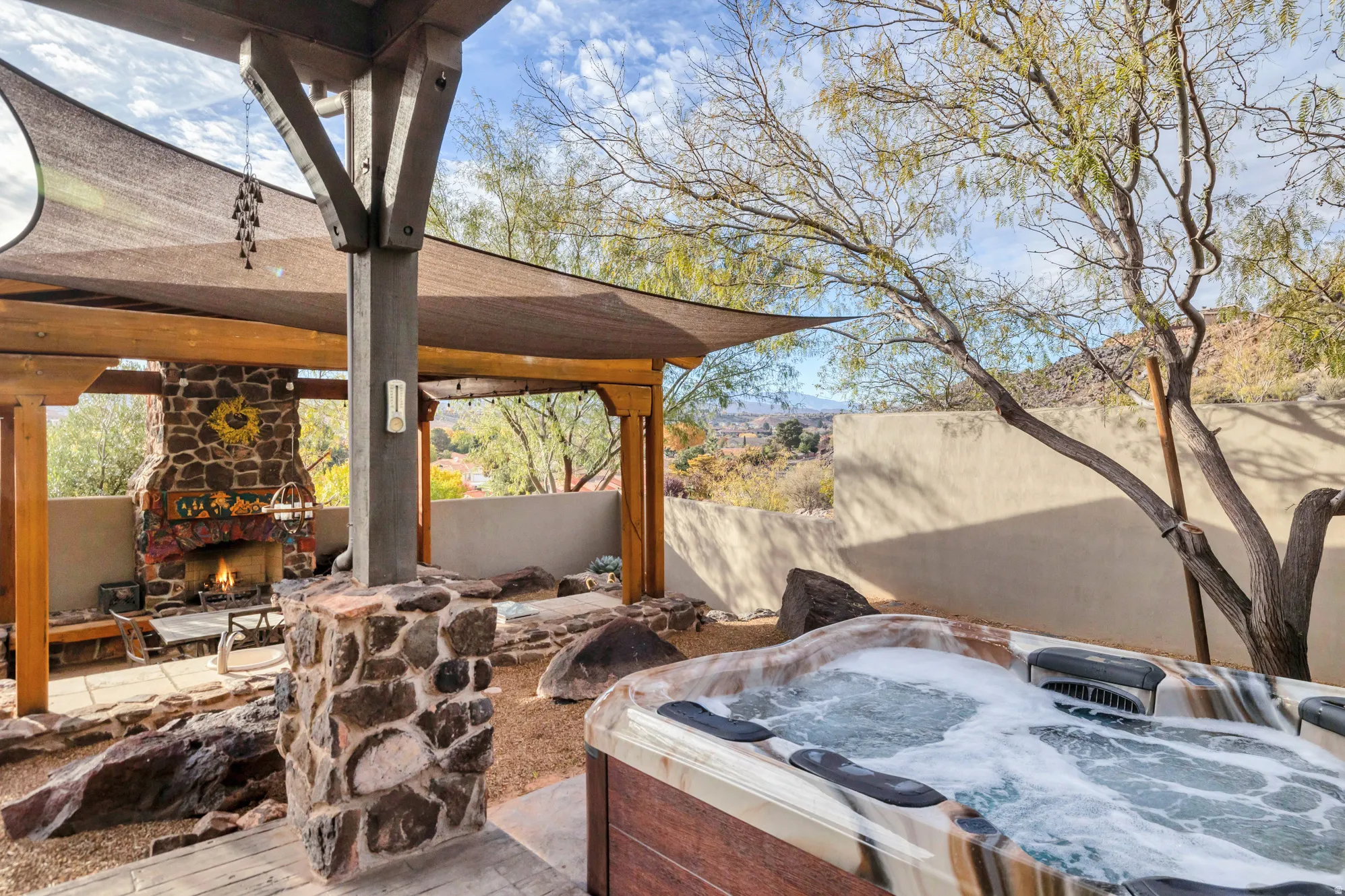 View of patio featuring an outdoor stone fireplace and a hot tub