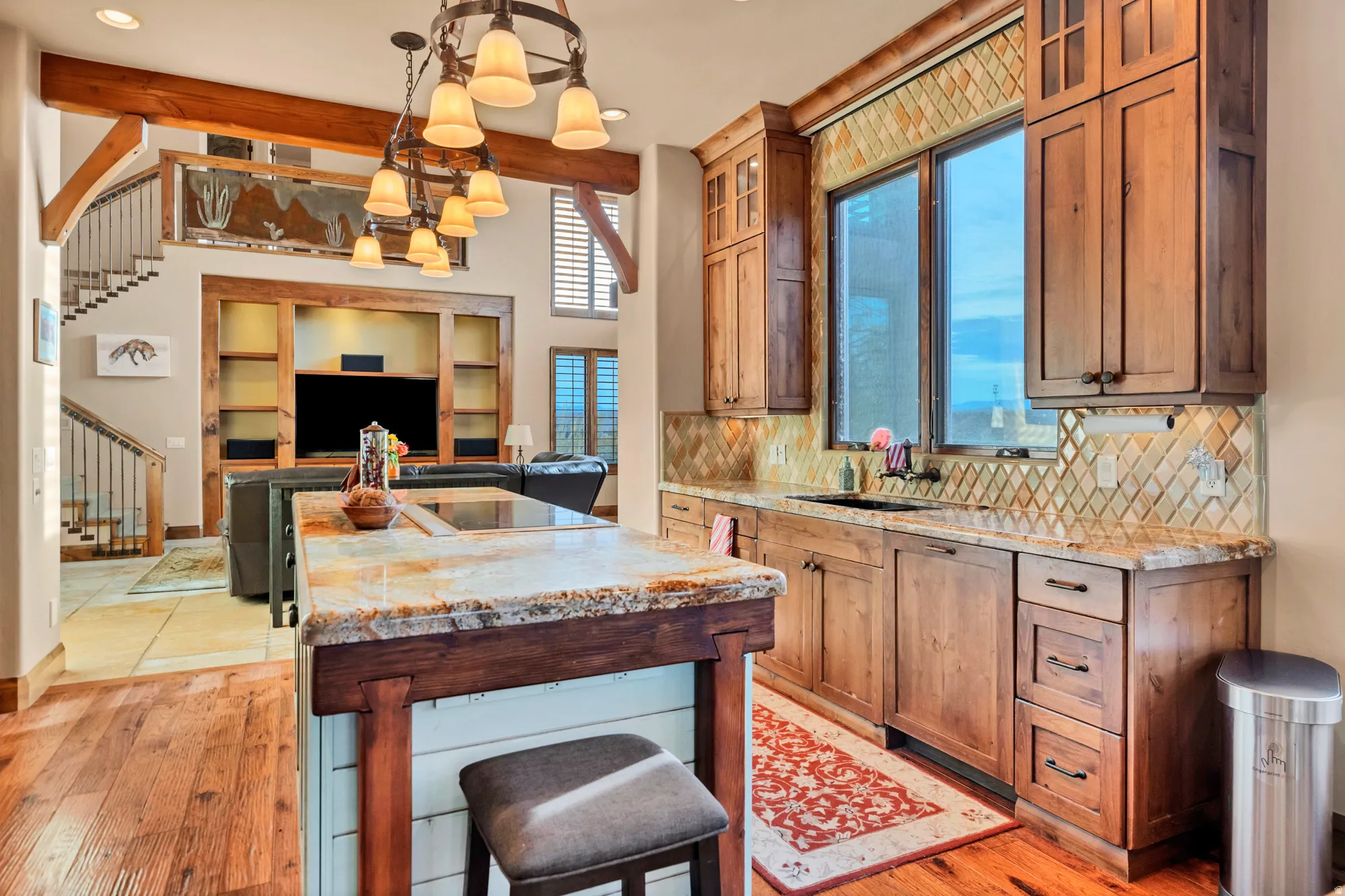 Kitchen with light stone countertops, decorative light fixtures, a center island, brown cabinets, and beam ceiling