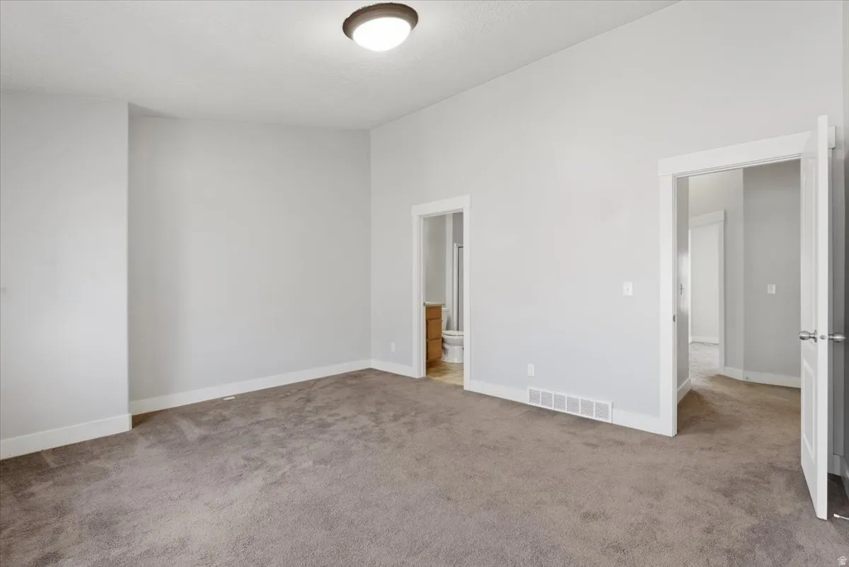 Unfurnished bedroom featuring light carpet, connected bathroom, and a high ceiling
