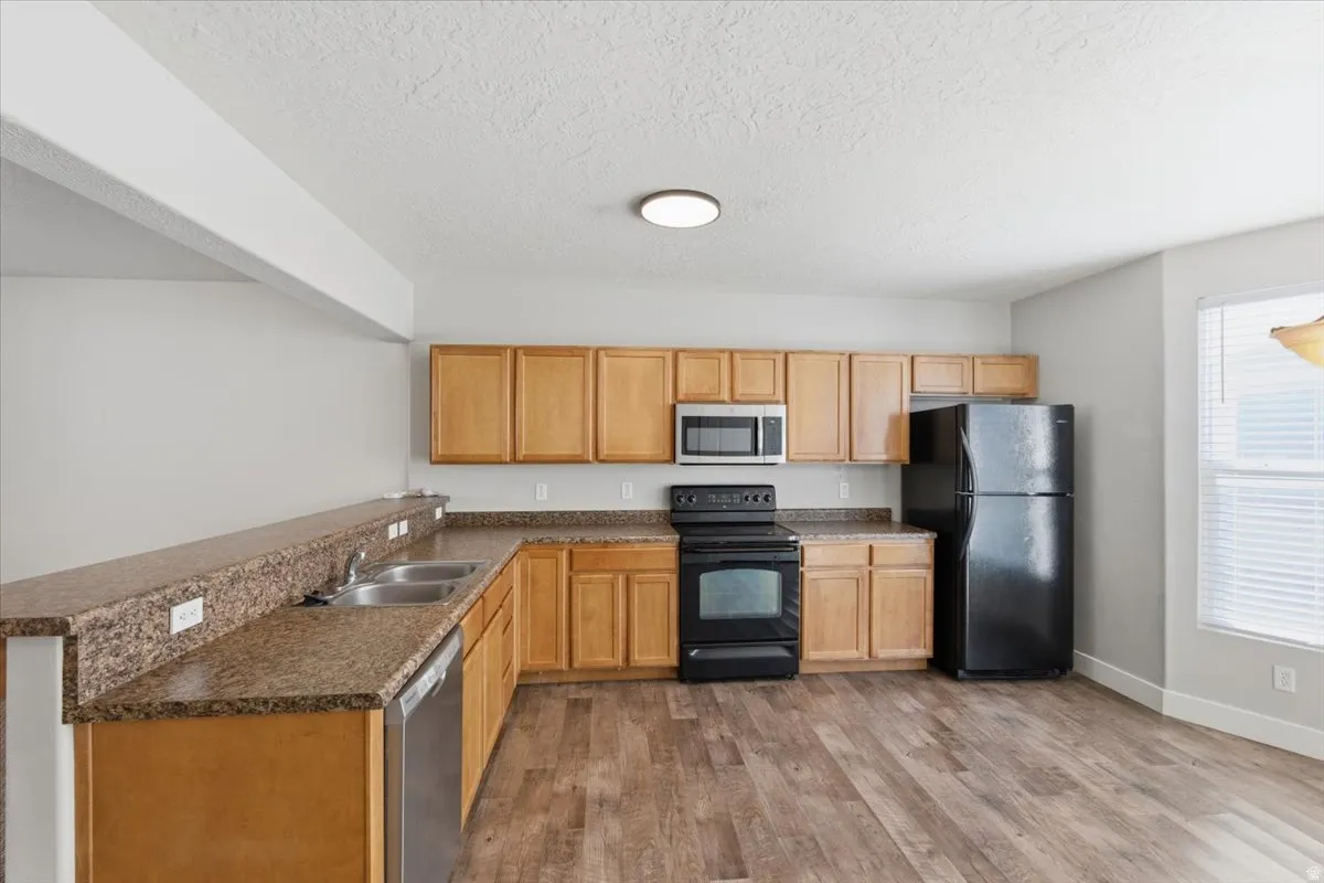 Kitchen featuring black appliances, a textured ceiling, light wood-style floors, and a peninsula