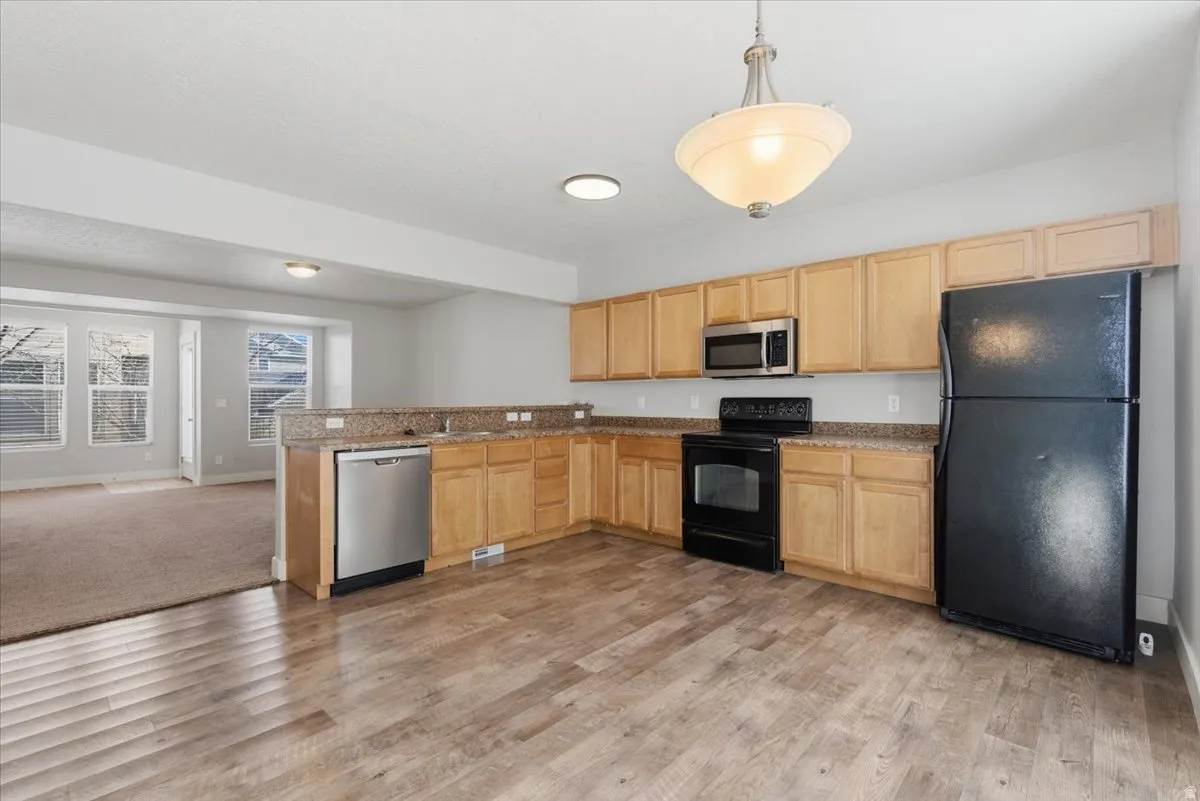 Kitchen with black appliances, light brown cabinets, pendant lighting, open floor plan, and a peninsula