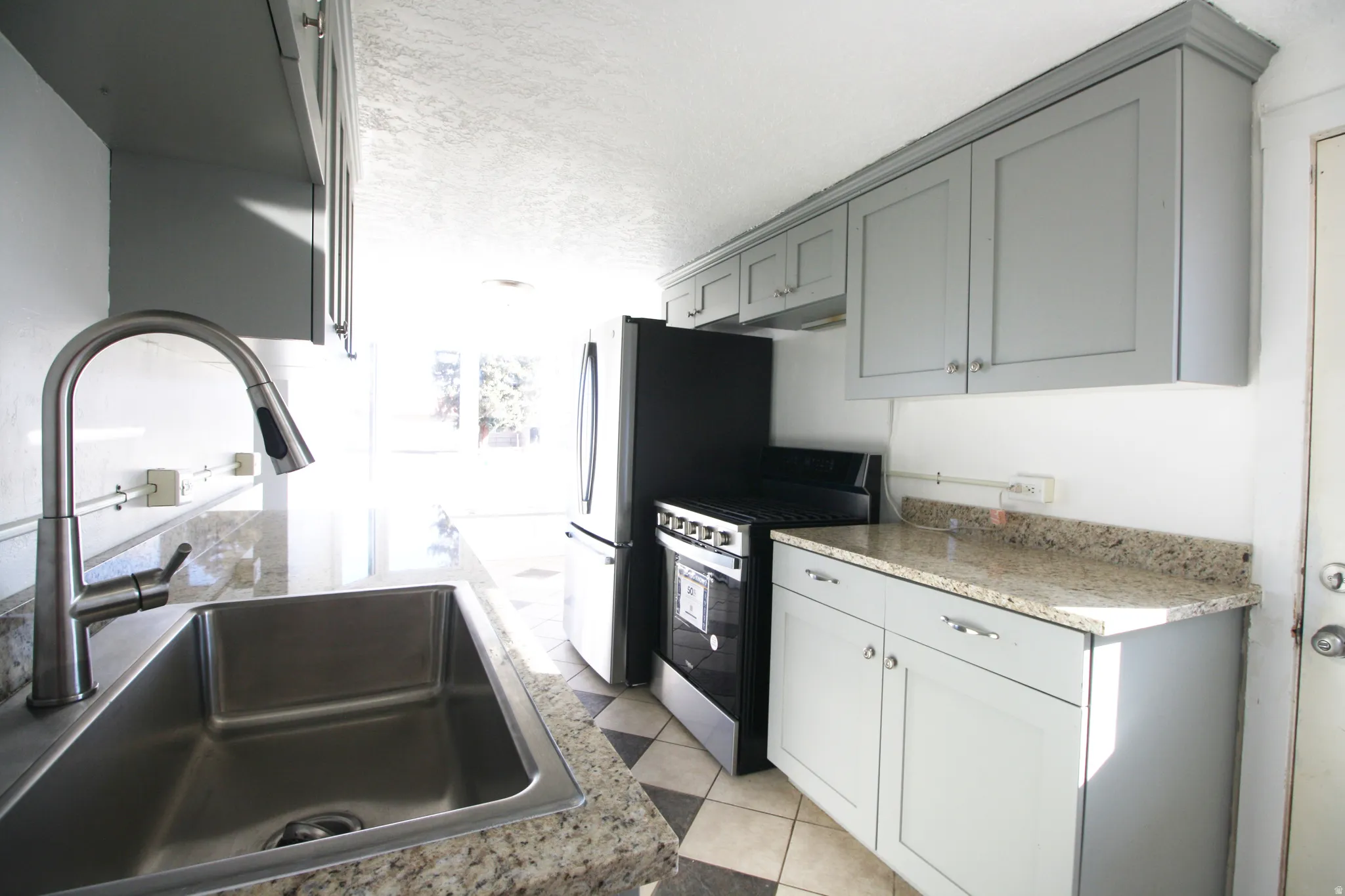 Kitchen with stainless steel range with gas stovetop, a textured ceiling, light stone countertops, and light tile patterned flooring