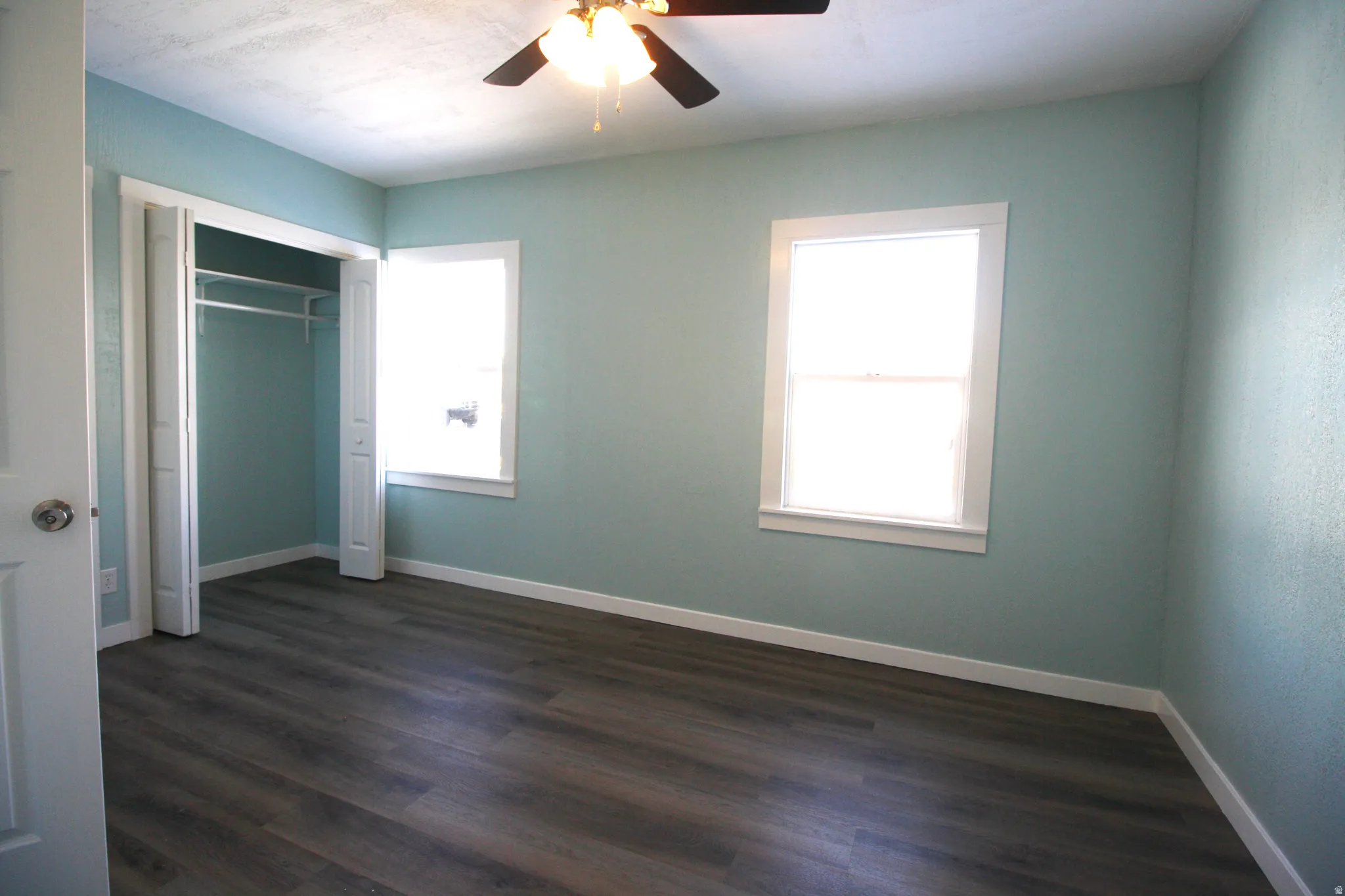 Master bedroom with dark wood-style flooring, a closet, ceiling fan, and multiple windows