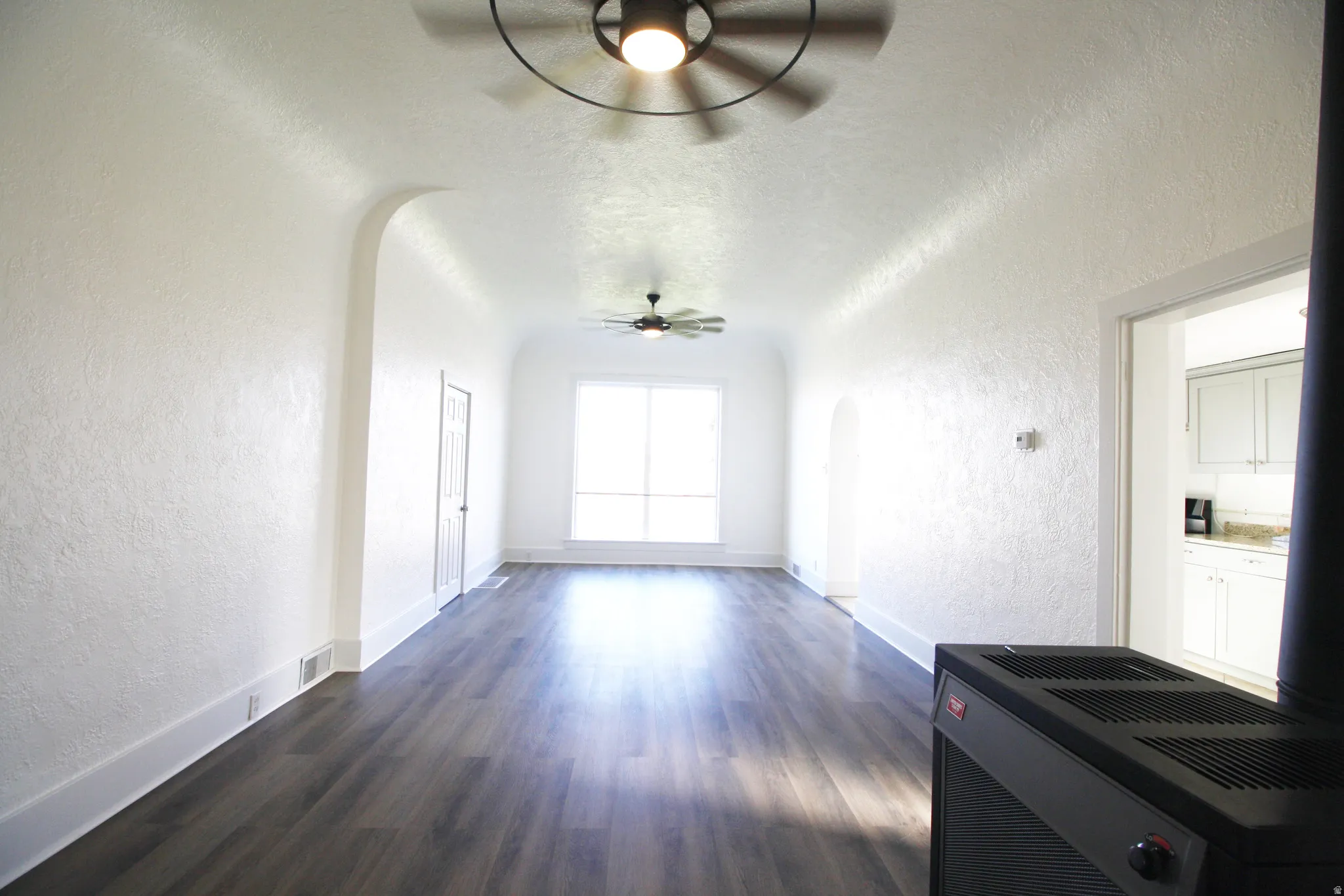 Family Room featuring a textured wall, arched walkways, dark wood-style flooring, a ceiling fan, and a textured ceiling