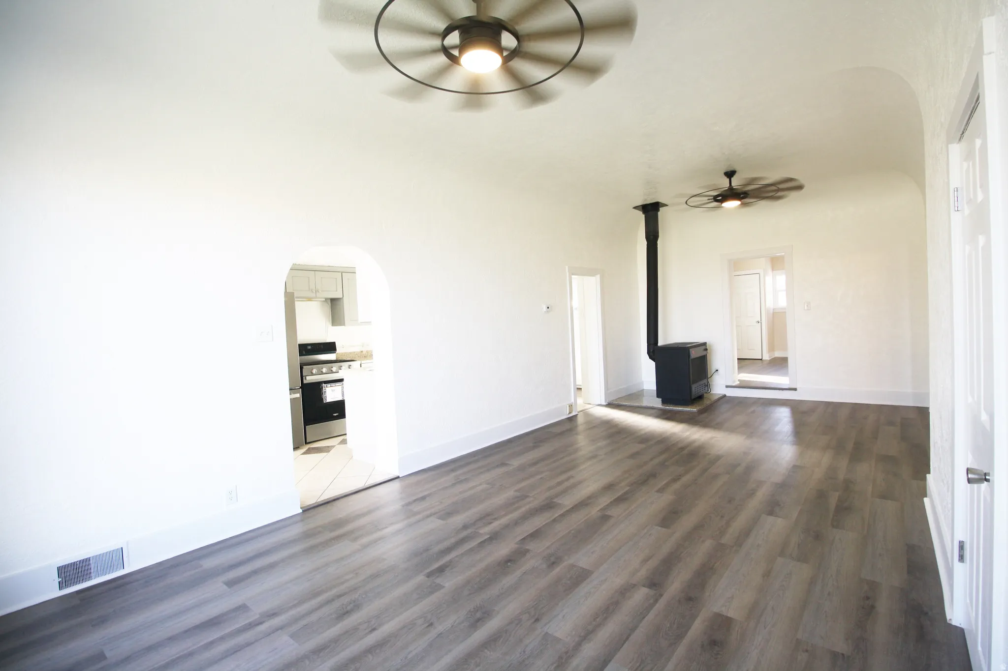 Family room with arched walkways, ceiling fan, a wood stove, and dark wood finished floors