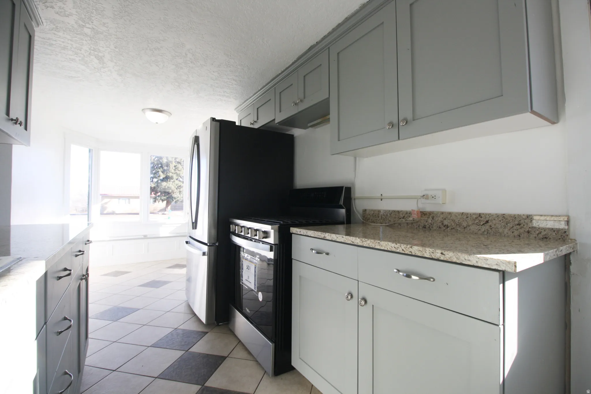 Kitchen with stainless steel range with electric stovetop, a textured ceiling, light stone countertops, and gray cabinetry