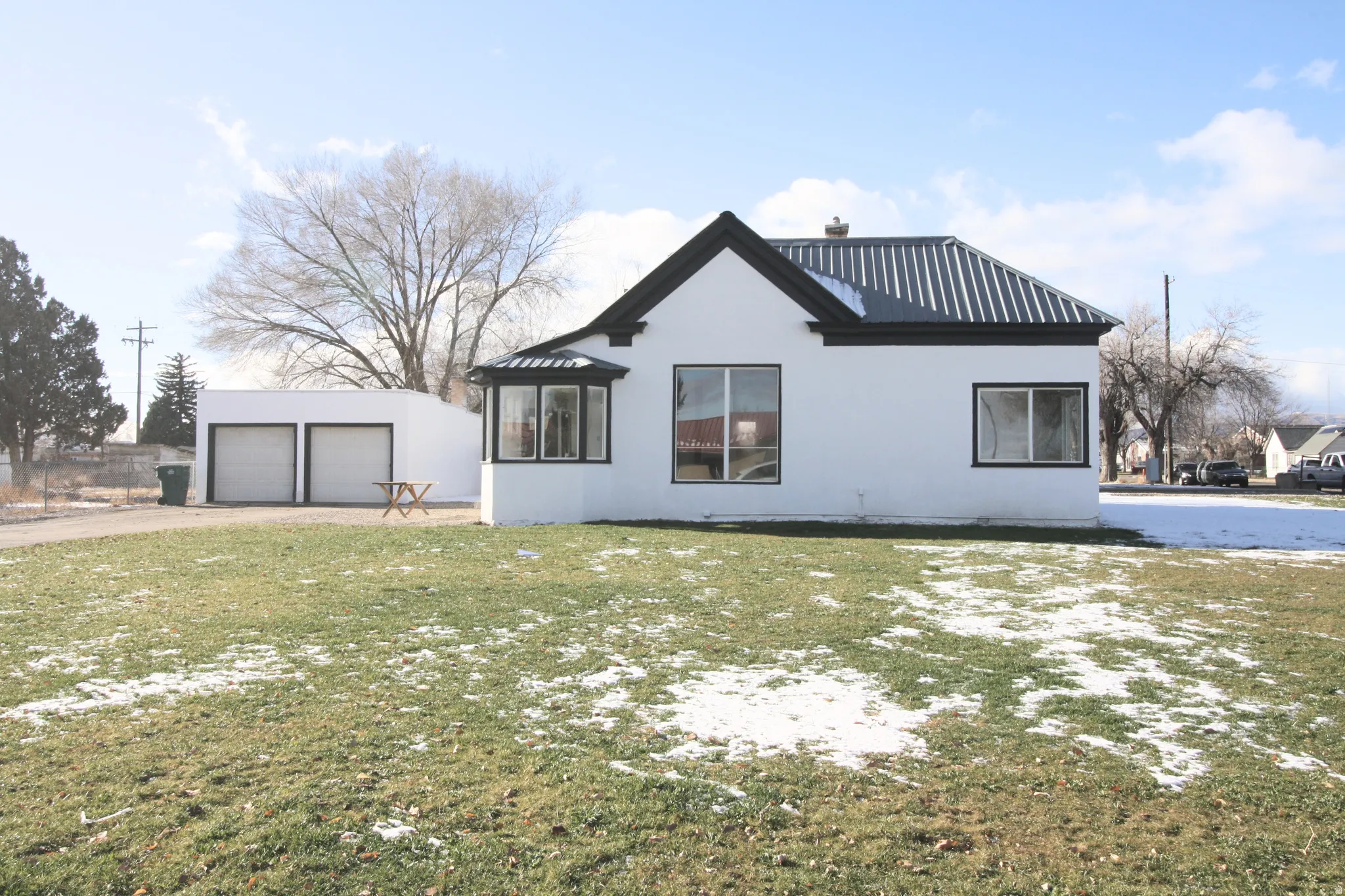 View of snowy exterior with a detached garage, a metal roof, stucco siding, and a yard