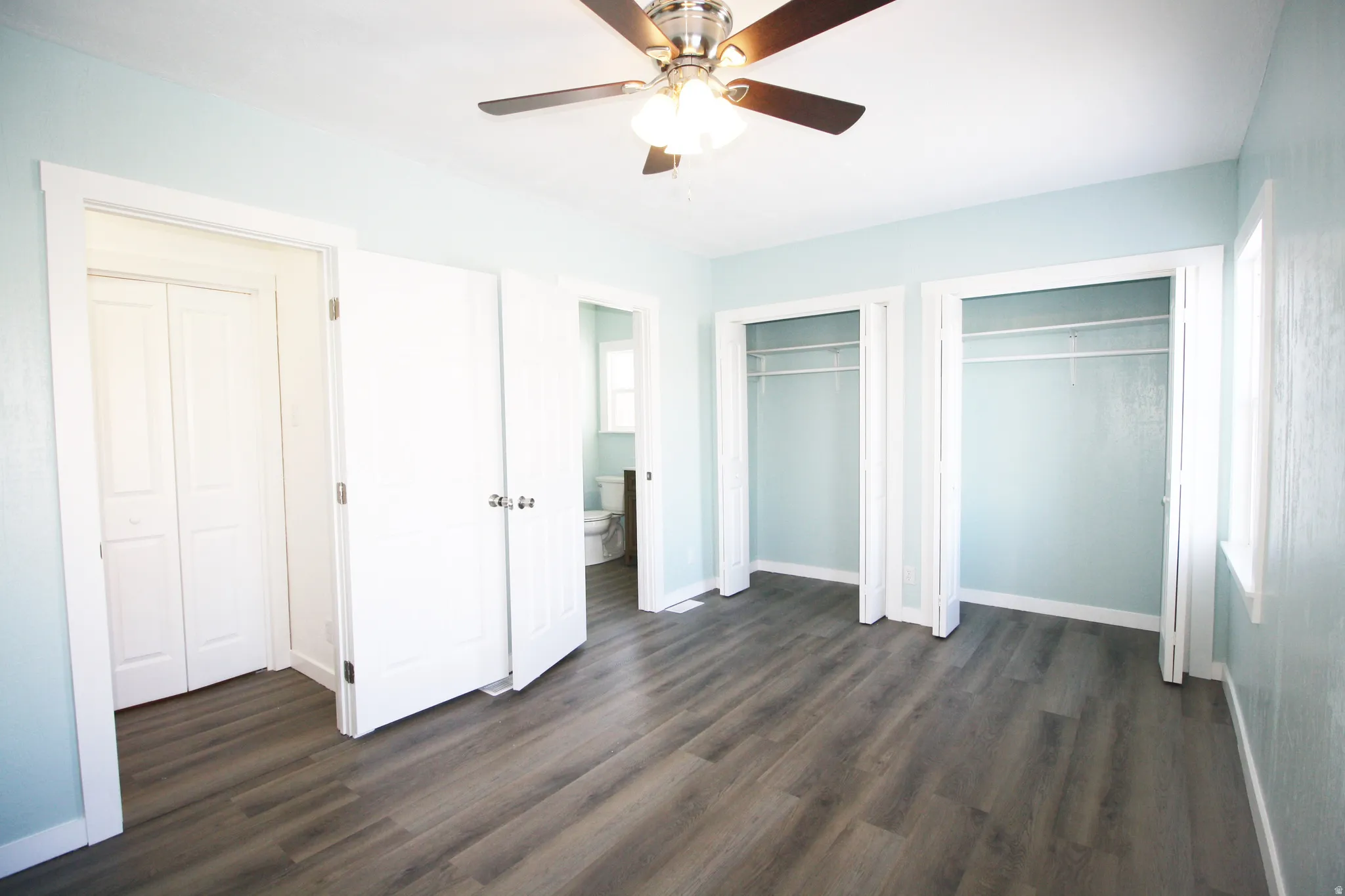 Master bedroom with two closets, dark wood finished floors, and ceiling fan