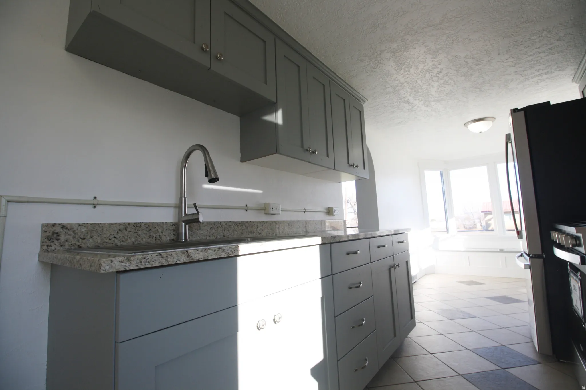 Kitchen featuring a textured ceiling, gray cabinetry, appliances with stainless steel finishes, light stone countertops, and light tile patterned floors