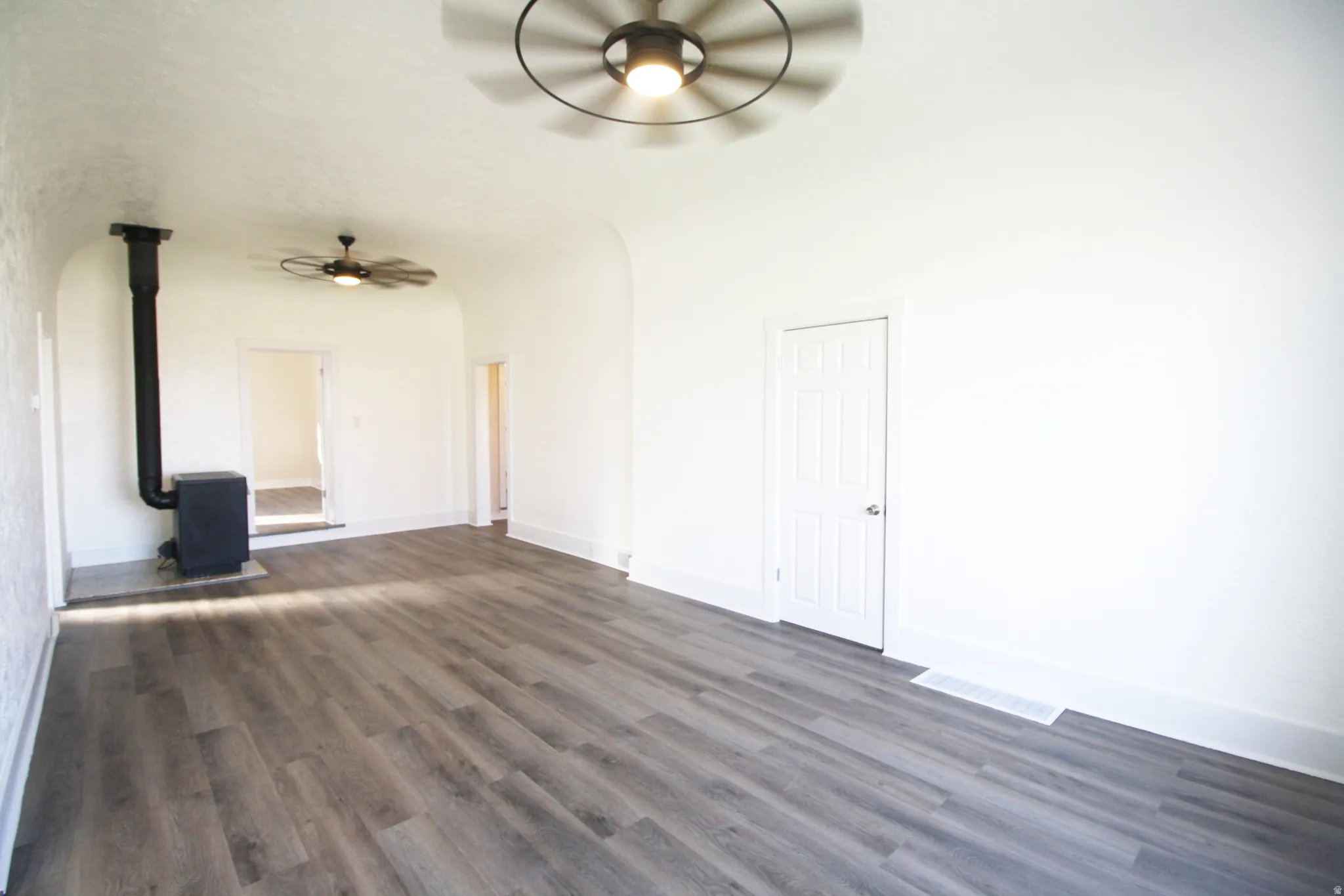 Family room with arched walkways, dark wood finished floors, ceiling fan, and a wood stove