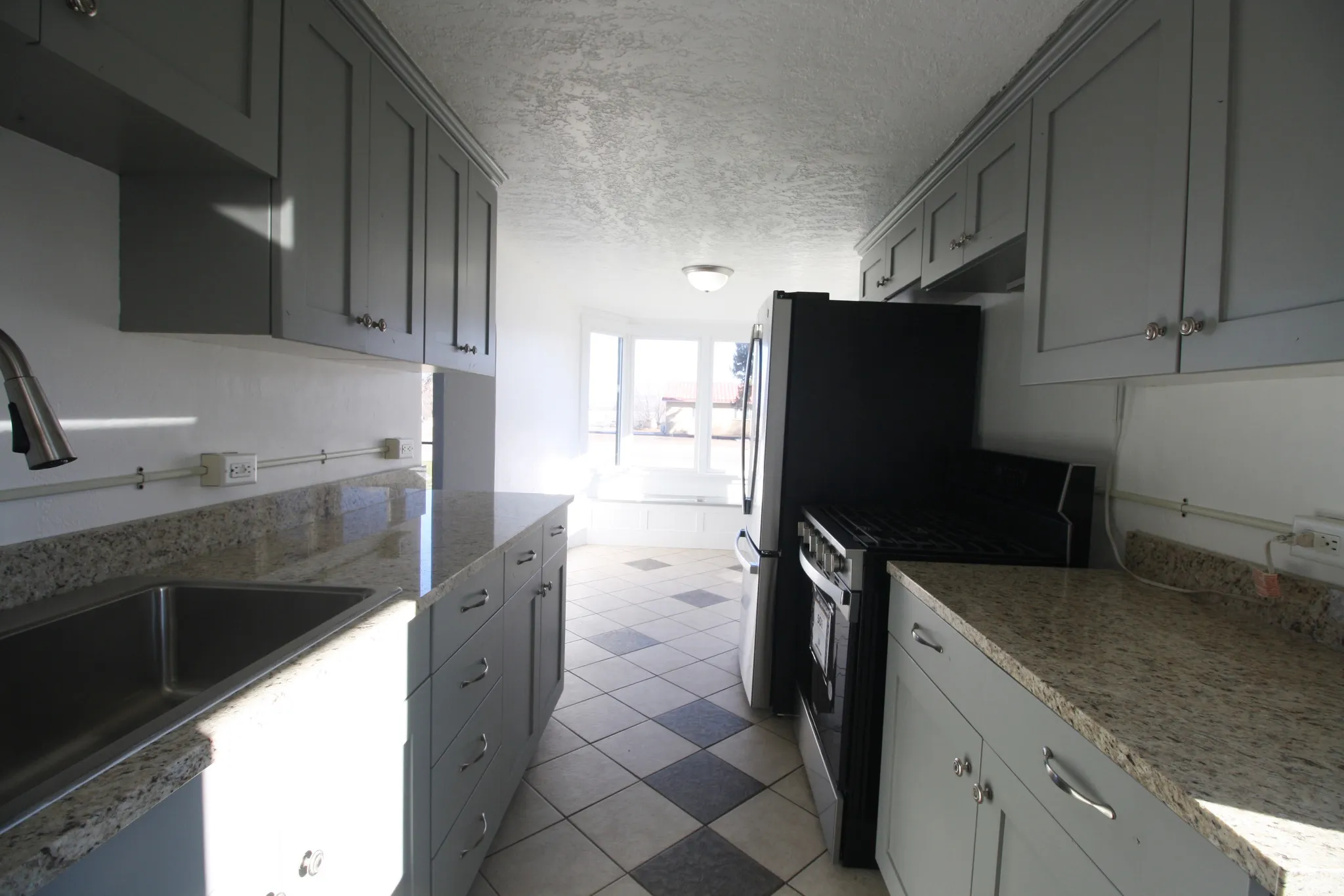 Kitchen with stainless steel gas range oven, a textured ceiling, light stone counters, and gray cabinetry