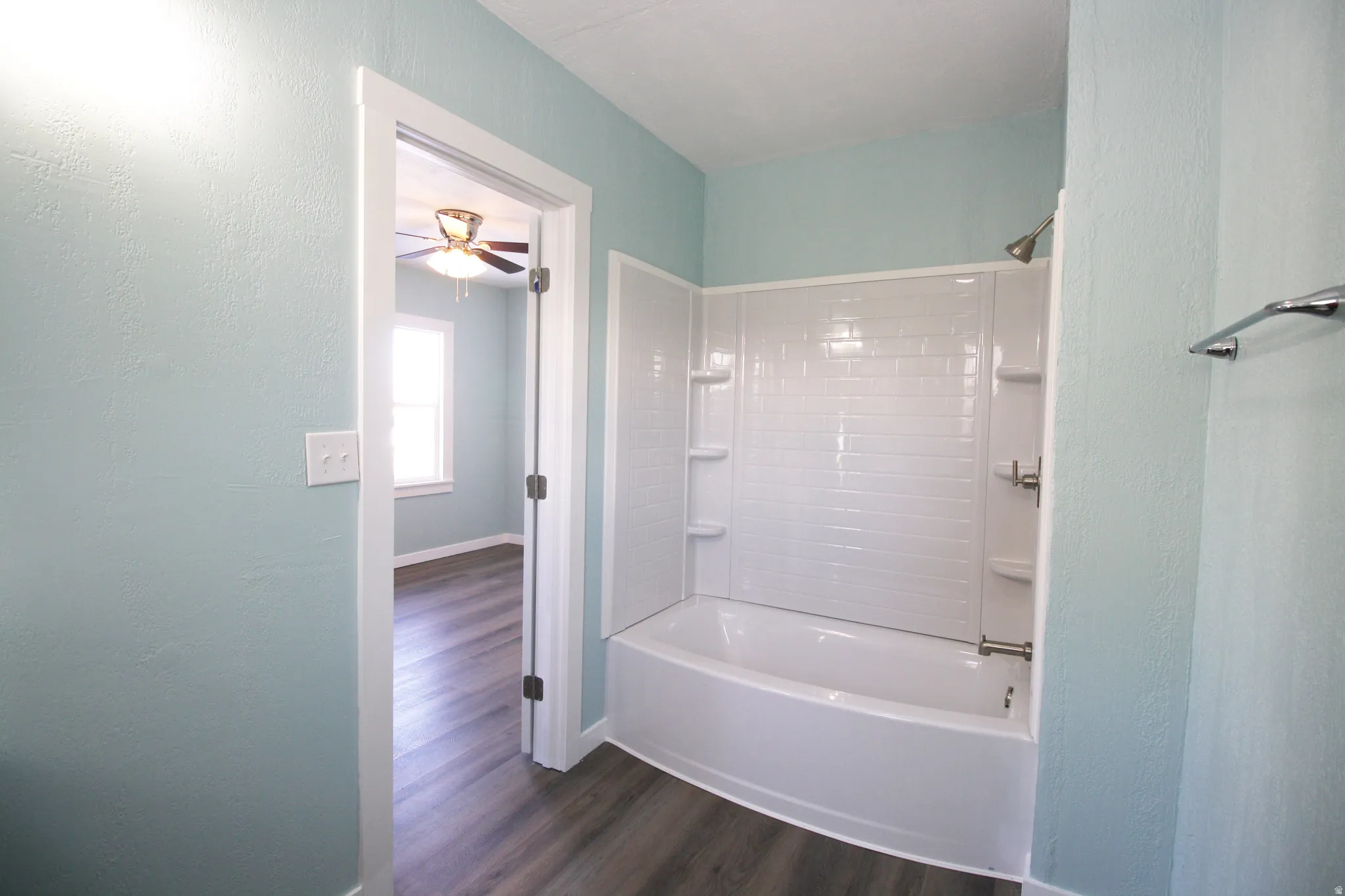 Master en-suite Bathroom with a textured wall, shower / bath combination, and dark wood-style floors