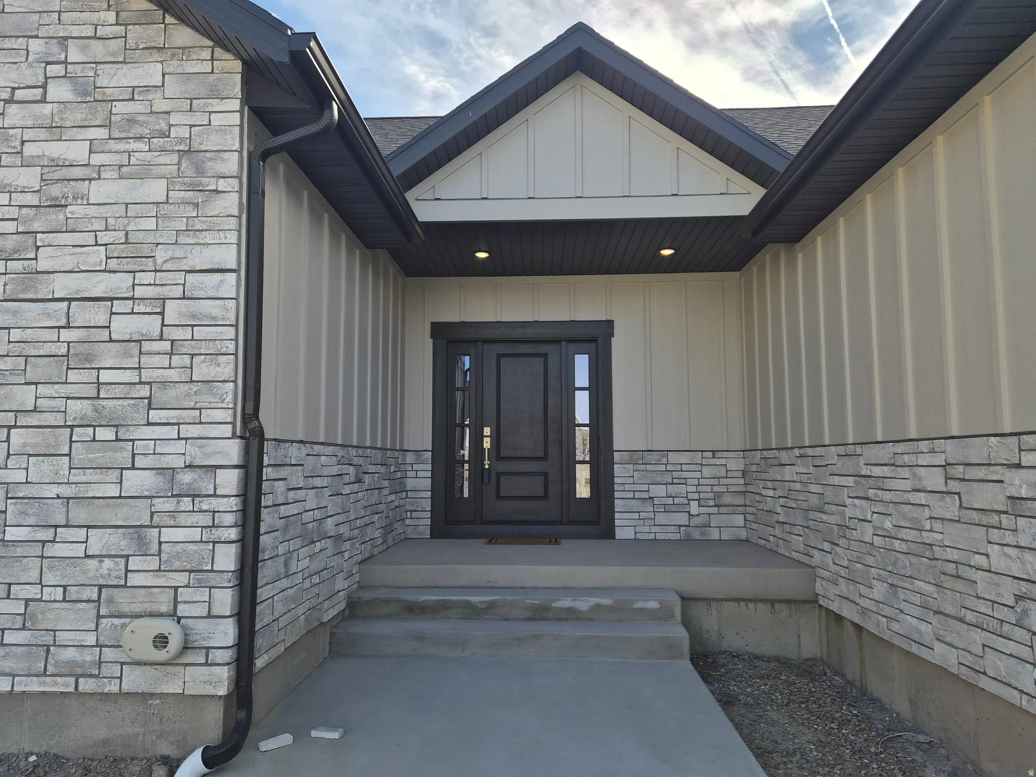 Doorway to property with stone siding, board and batten siding, and a shingled roof