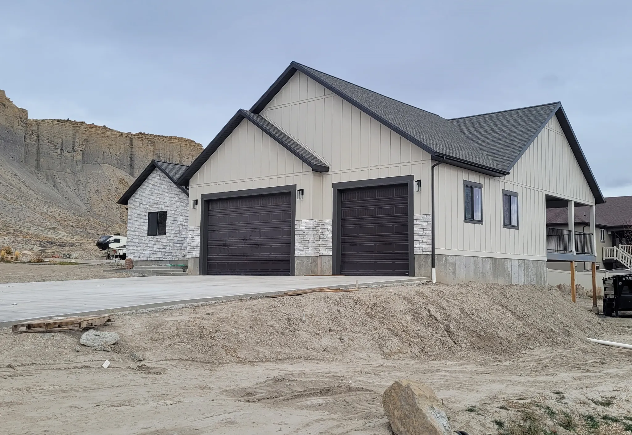 View of front of property featuring board and batten siding, roof with shingles, driveway, an attached garage, and stone siding