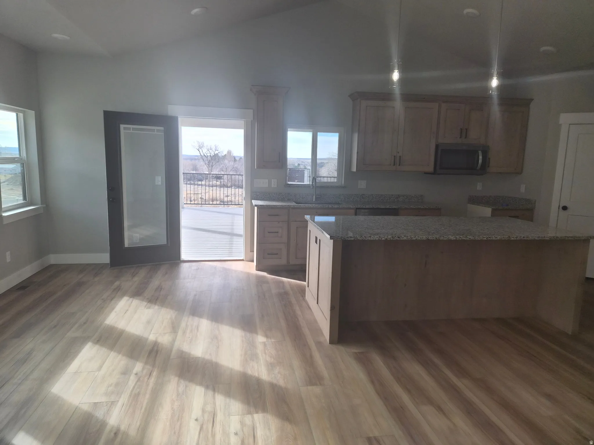 Kitchen with stainless steel microwave, vaulted ceiling, light stone countertops, light wood-style flooring, and wood finish cabinetry