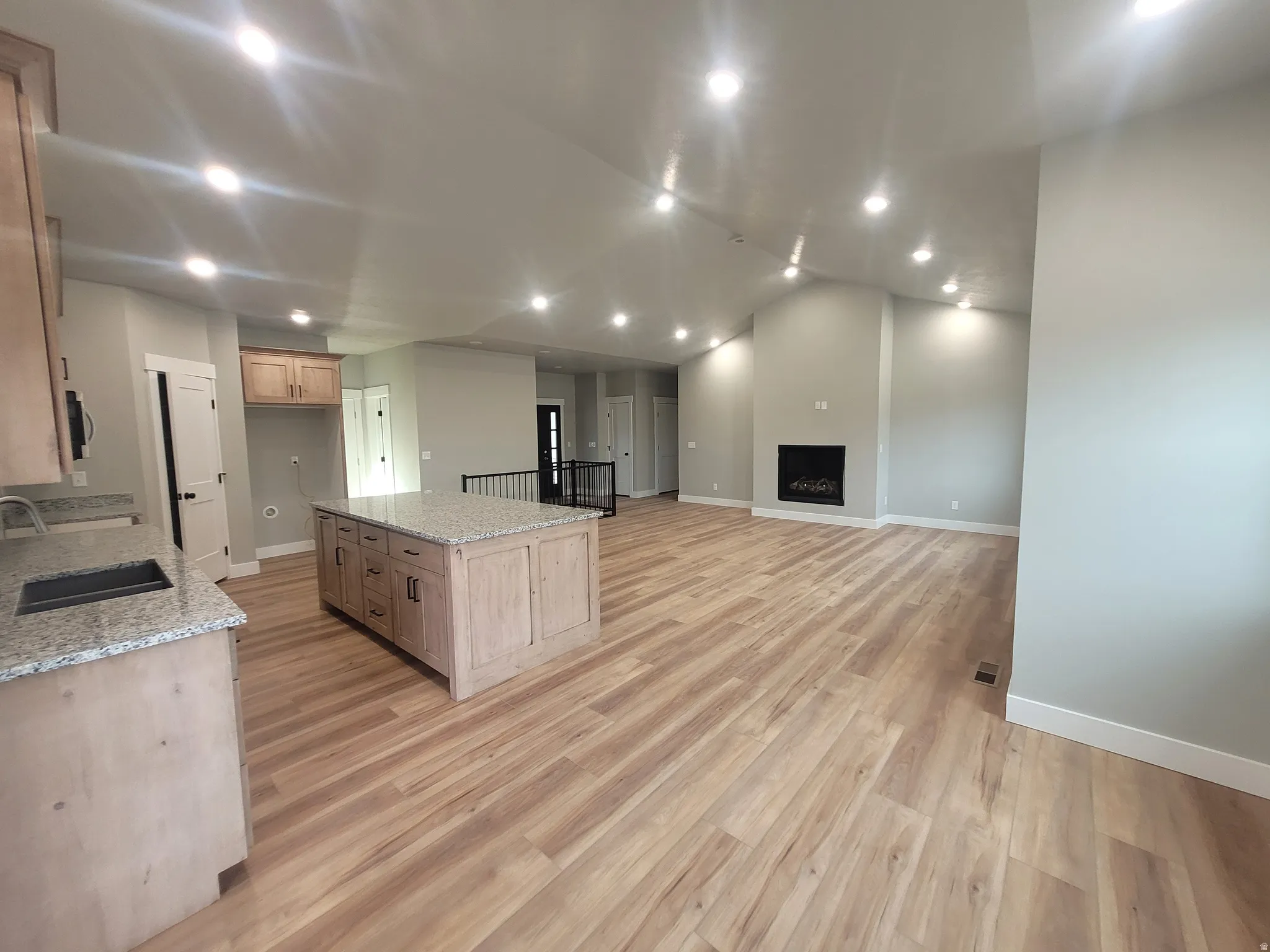 Kitchen featuring recessed lighting, light stone counters, a kitchen island, light brown cabinetry, and a fireplace