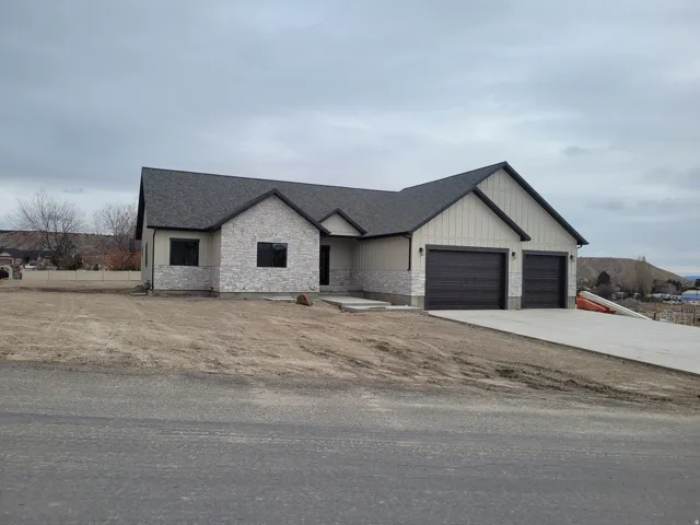 View of front of home featuring stone siding, a shingled roof, concrete driveway, and board and batten siding