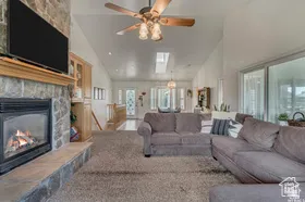 Living area featuring a fireplace, high vaulted ceiling, a ceiling fan, and a skylight