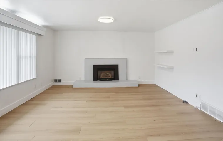 Unfurnished living room featuring a fireplace with raised hearth and light wood-type flooring