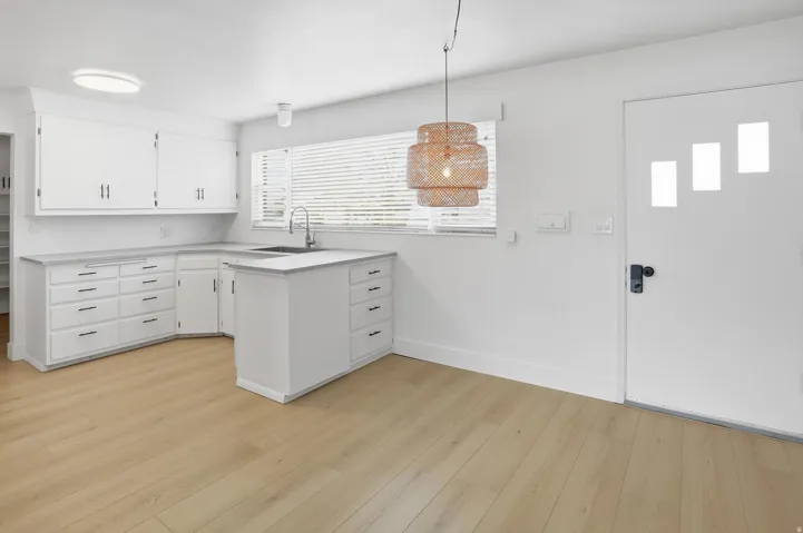 Kitchen featuring decorative light fixtures, light countertops, white cabinets, and light wood-style floors