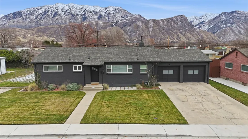 View of front of home with a front lawn, a mountain view, driveway, roof with shingles, and brick siding