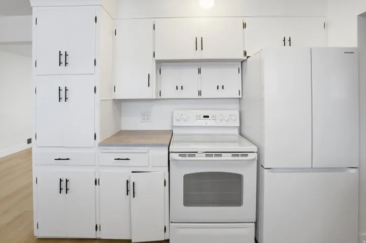 Kitchen featuring white appliances, white cabinetry, and light countertops