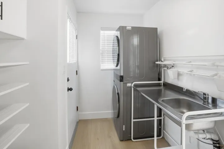 Washroom with stacked washer and clothes dryer and light wood finished floors