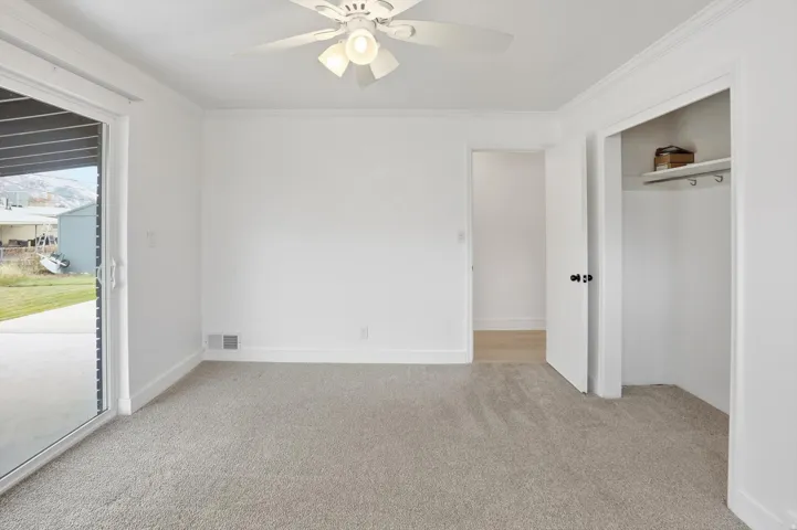 Unfurnished bedroom with light colored carpet, access to exterior, ornamental molding, a ceiling fan, and a closet