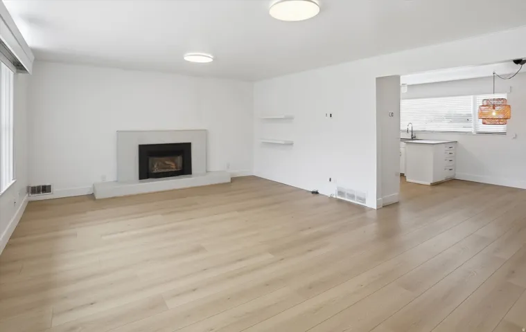 Unfurnished living room with a fireplace with raised hearth and light wood-type flooring