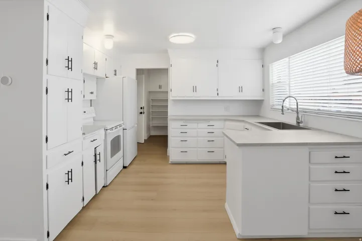 Kitchen featuring white electric range oven, light countertops, white cabinets, a peninsula, and light wood-style flooring