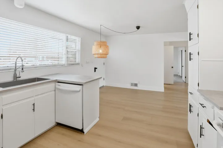 Kitchen with white cabinets, light countertops, white dishwasher, and light wood finished floors