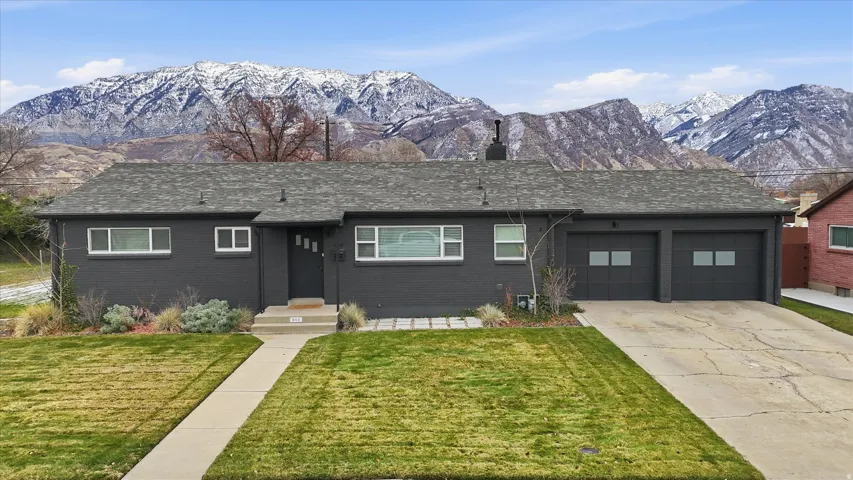 View of front facade featuring a mountain view, a front yard, an attached garage, brick siding, and driveway