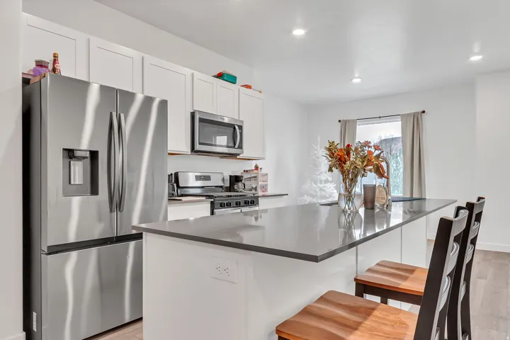 Kitchen featuring stainless steel appliances, light wood-style floors, white cabinetry, a center island, and a kitchen breakfast bar