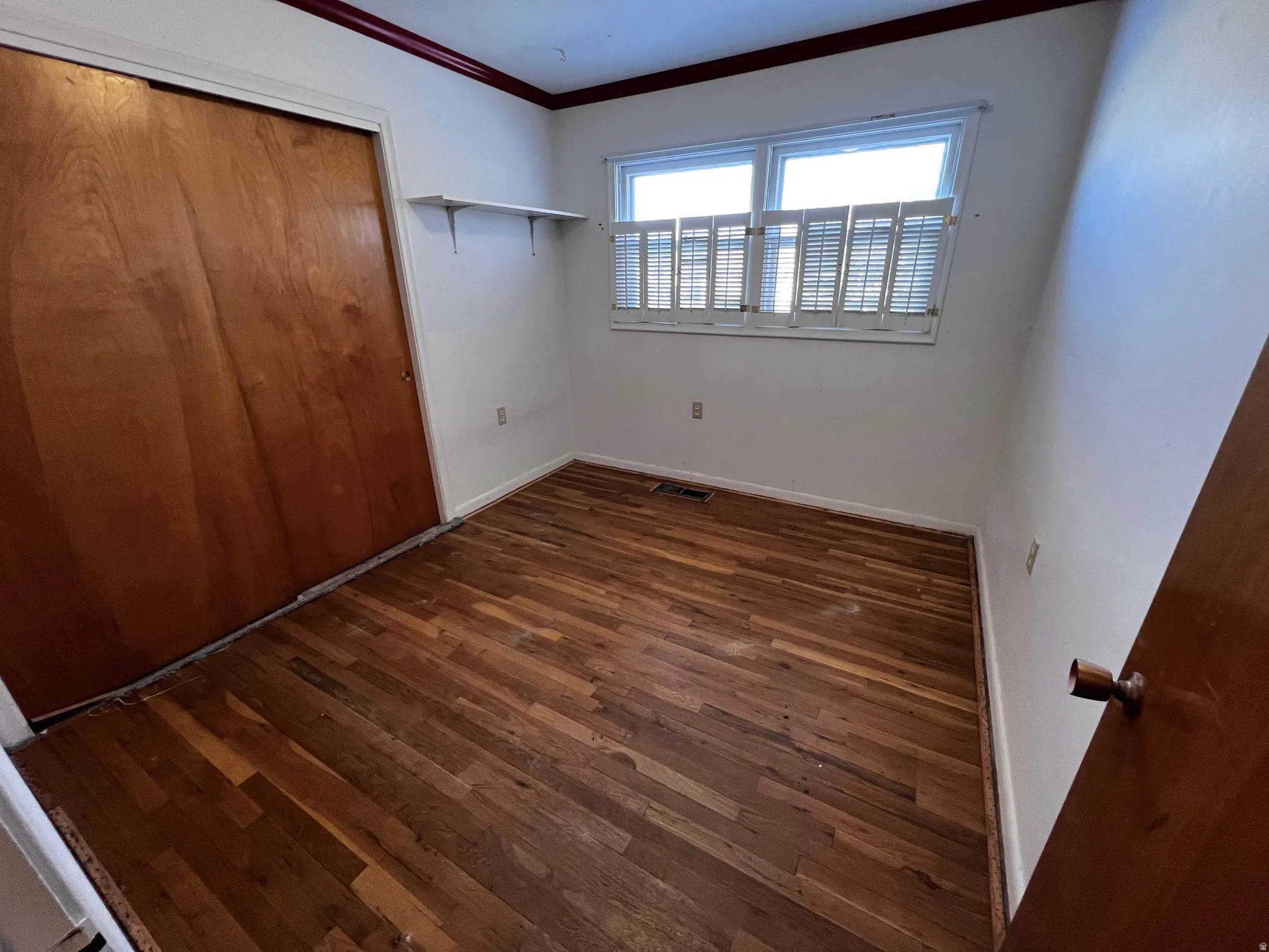 Unfurnished bedroom with a closet, ornamental molding, and dark wood finished floors