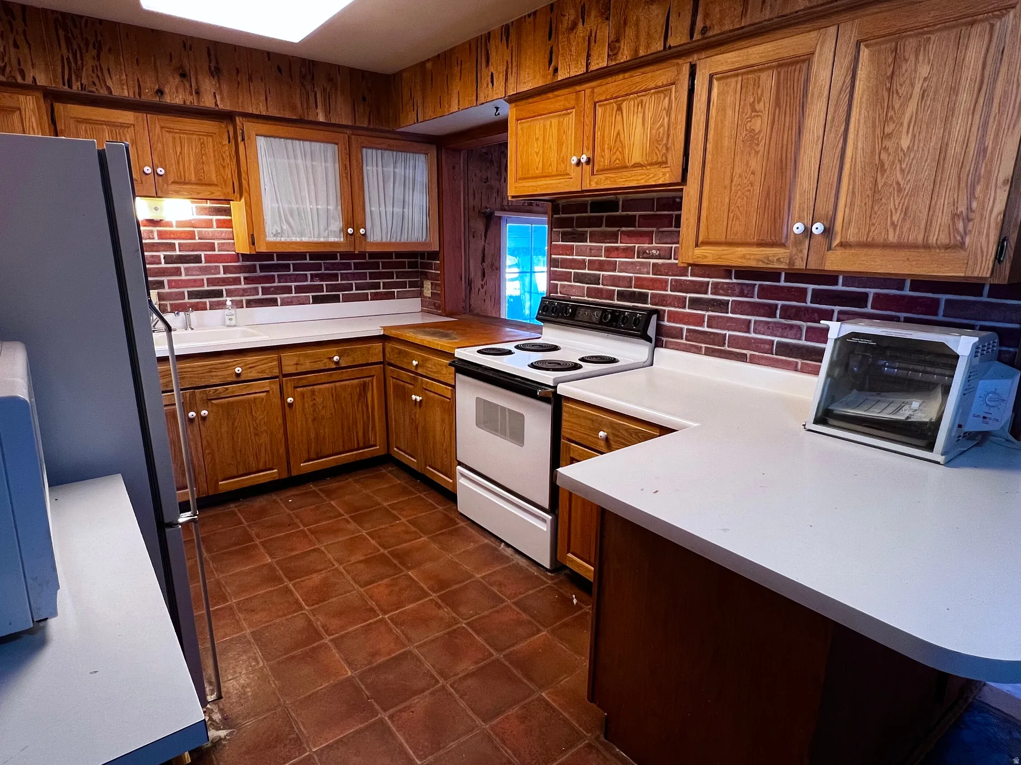 Kitchen featuring brown cabinets, white electric range oven, light countertops, freestanding refrigerator, and decorative backsplash