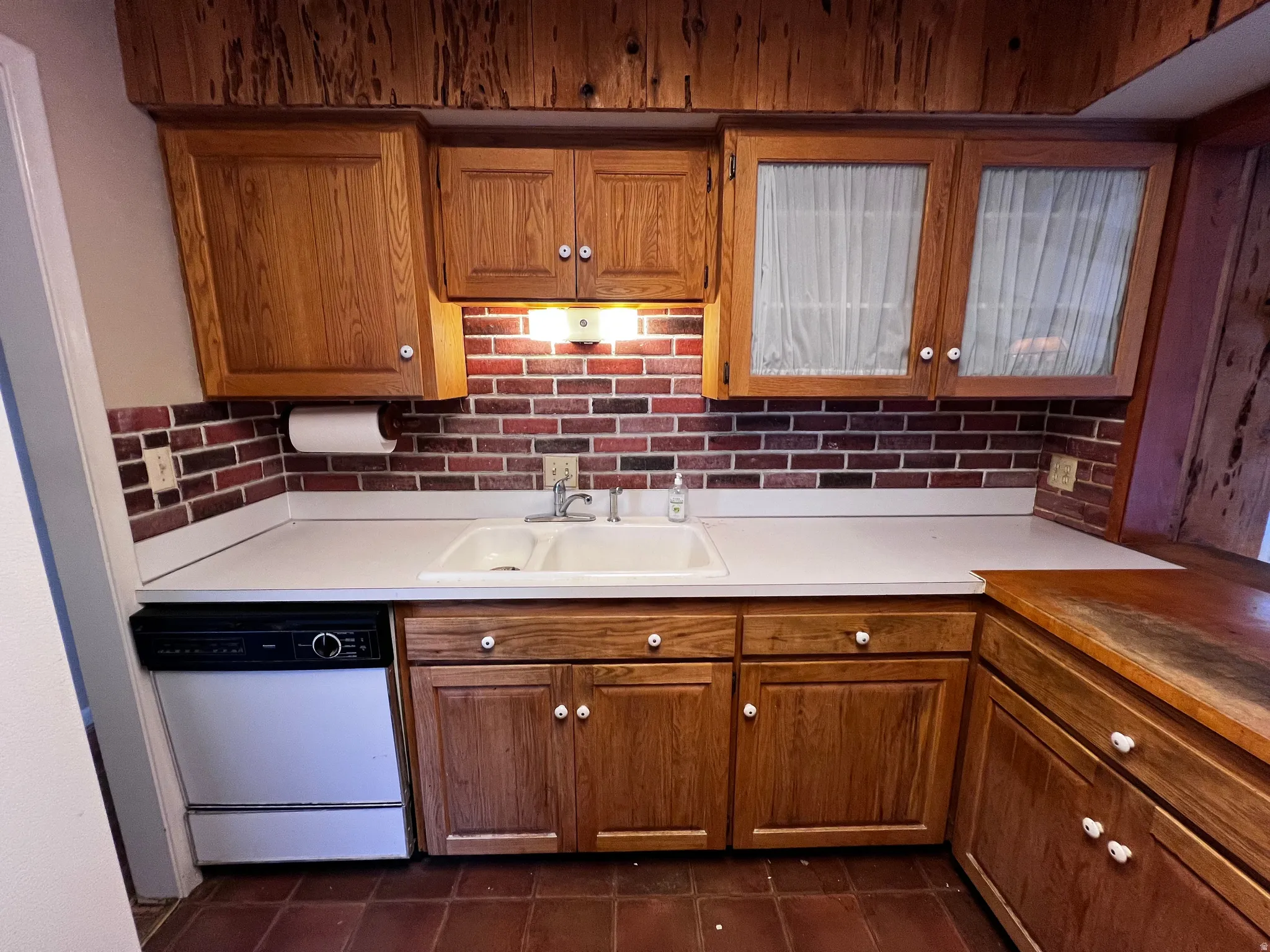 Kitchen with white dishwasher, brown cabinetry, and light countertops