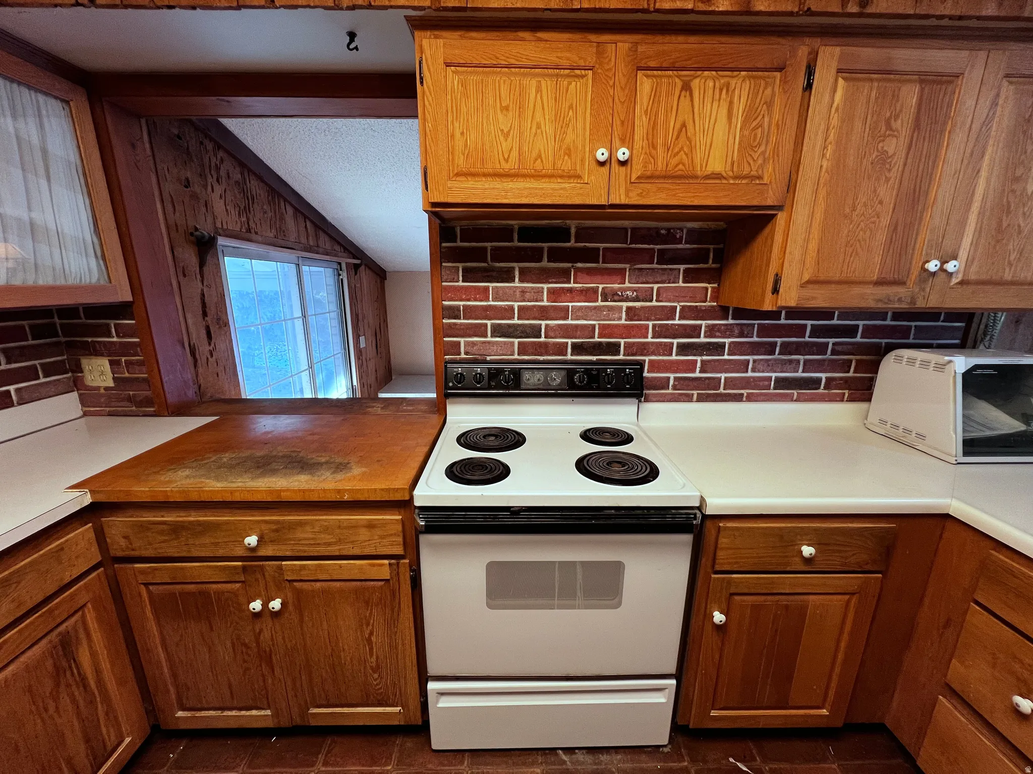 Kitchen with brown cabinets, white electric range oven, decorative backsplash, and light countertops