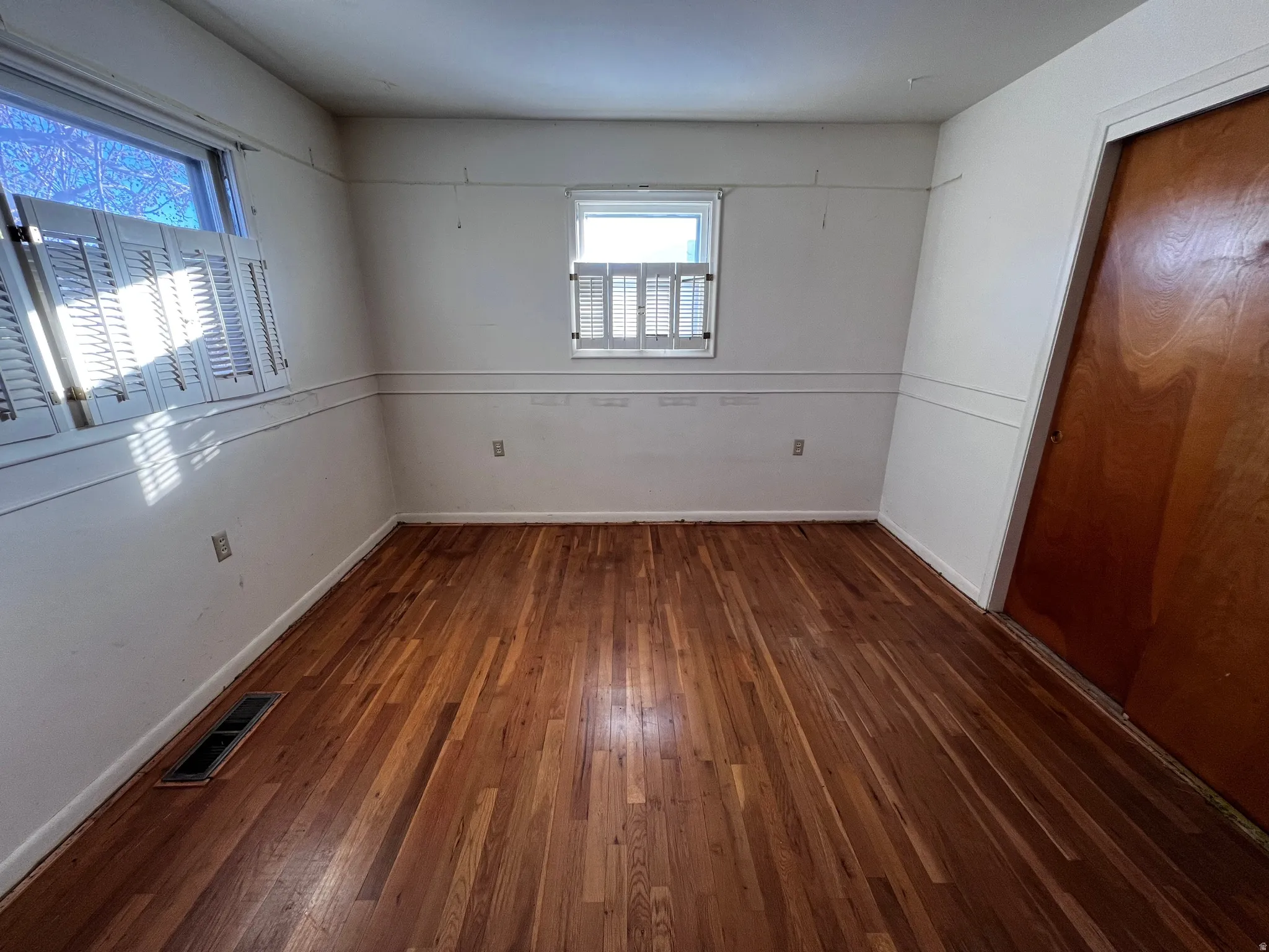 Unfurnished bedroom with multiple windows, dark wood finished floors, and a closet