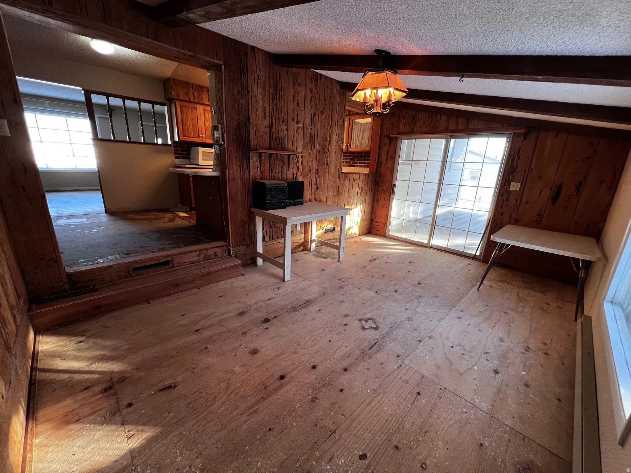 Unfurnished dining area featuring a textured ceiling, wooden walls, beam ceiling, and healthy amount of natural light