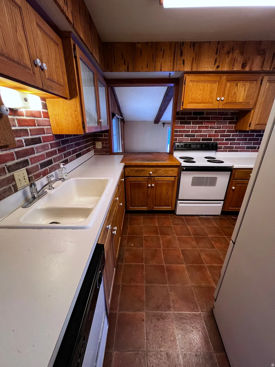 Kitchen featuring white appliances, brown cabinetry, light countertops, and decorative backsplash