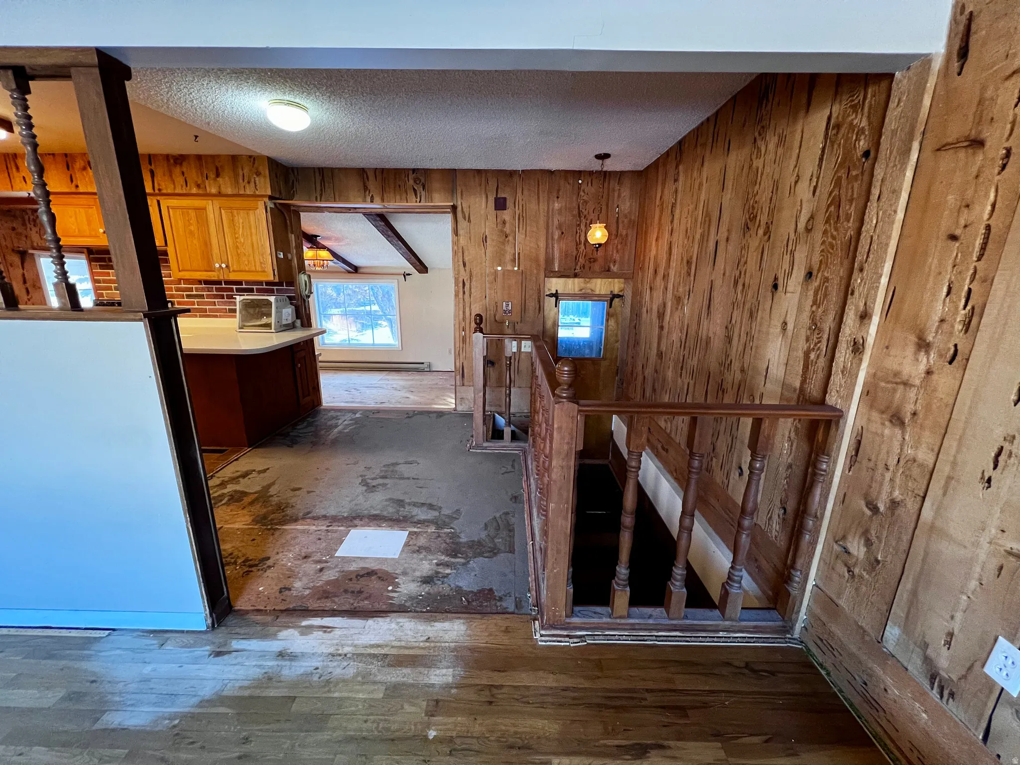 Hall with an upstairs landing, a textured ceiling, wooden walls, and dark wood-style floors