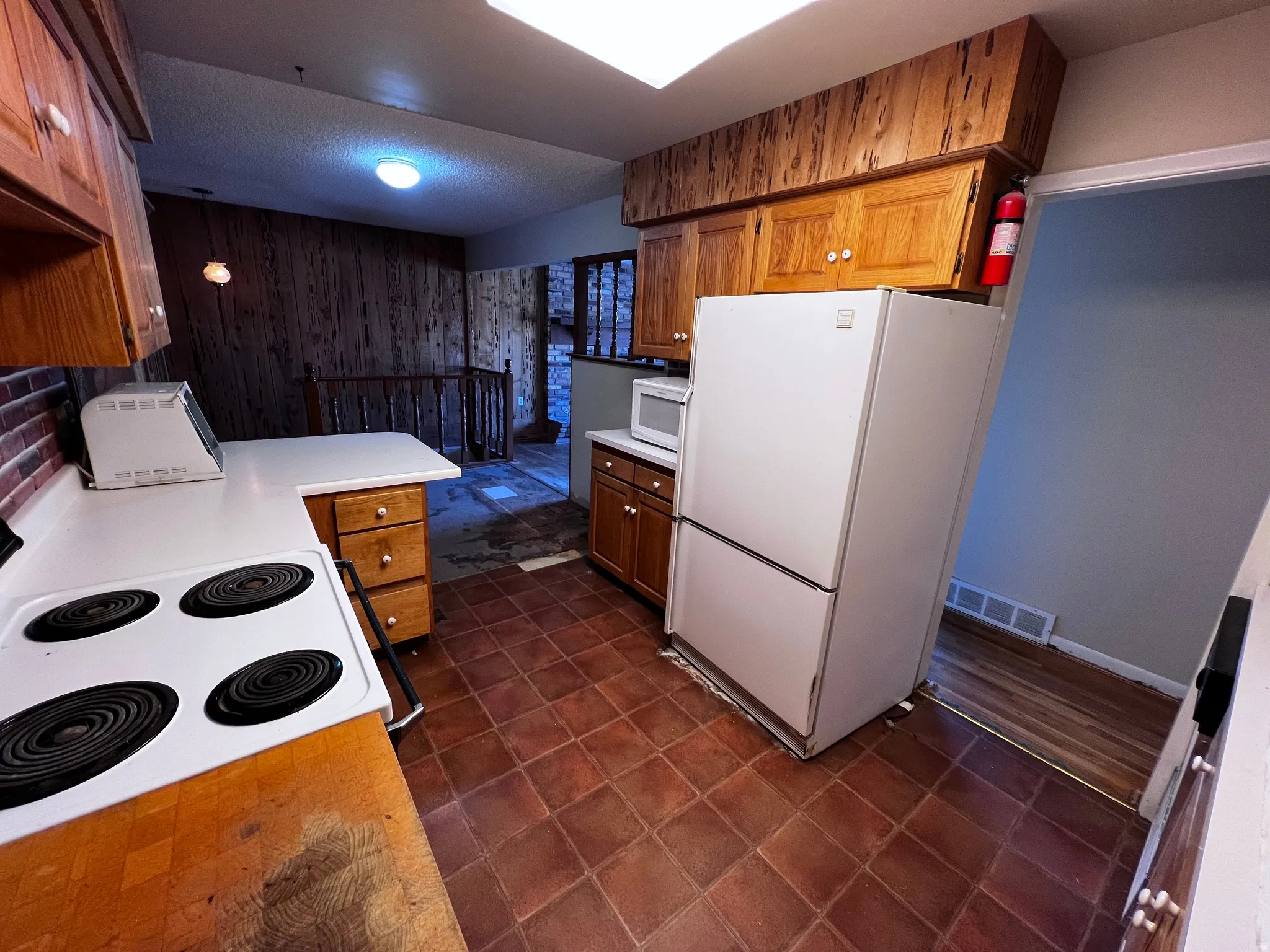 Kitchen featuring white appliances, light countertops, wooden walls, brown cabinets, and a textured ceiling