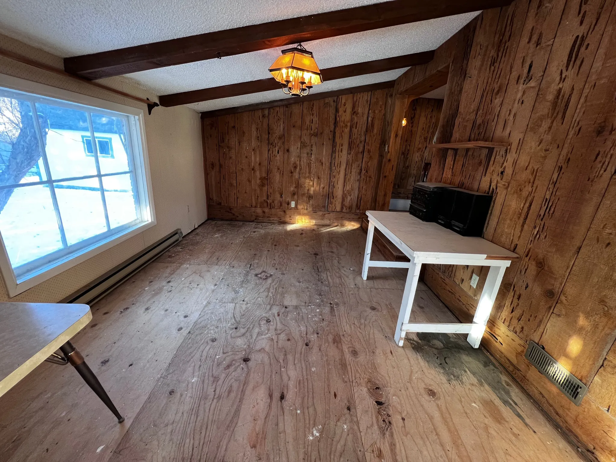 Unfurnished living room with wooden walls, a textured ceiling, a baseboard heating unit, and a chandelier