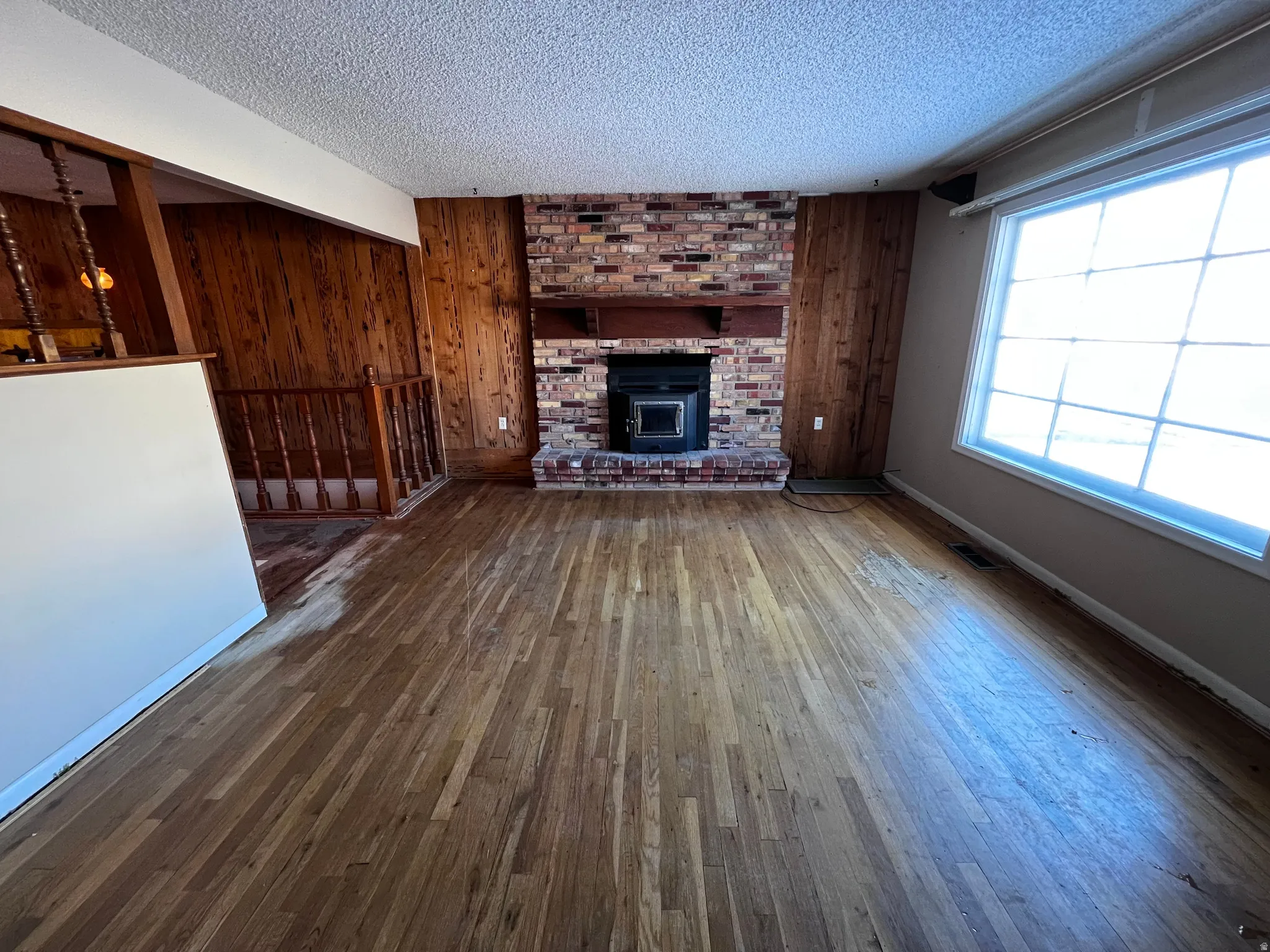 Unfurnished living room featuring wood walls, dark wood-style floors, and a textured ceiling