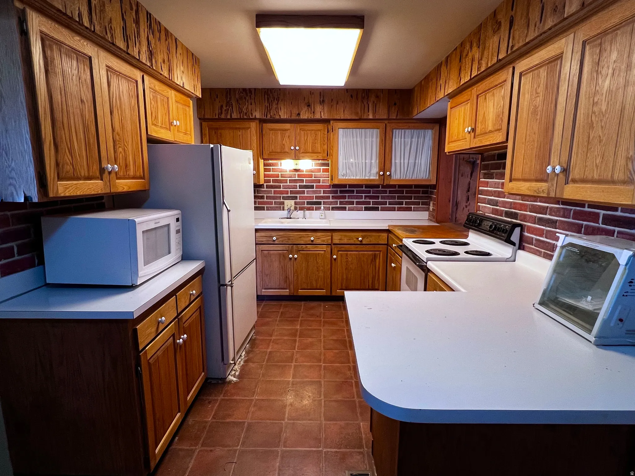 Kitchen with brown cabinets, white appliances, light countertops, a peninsula, and decorative backsplash